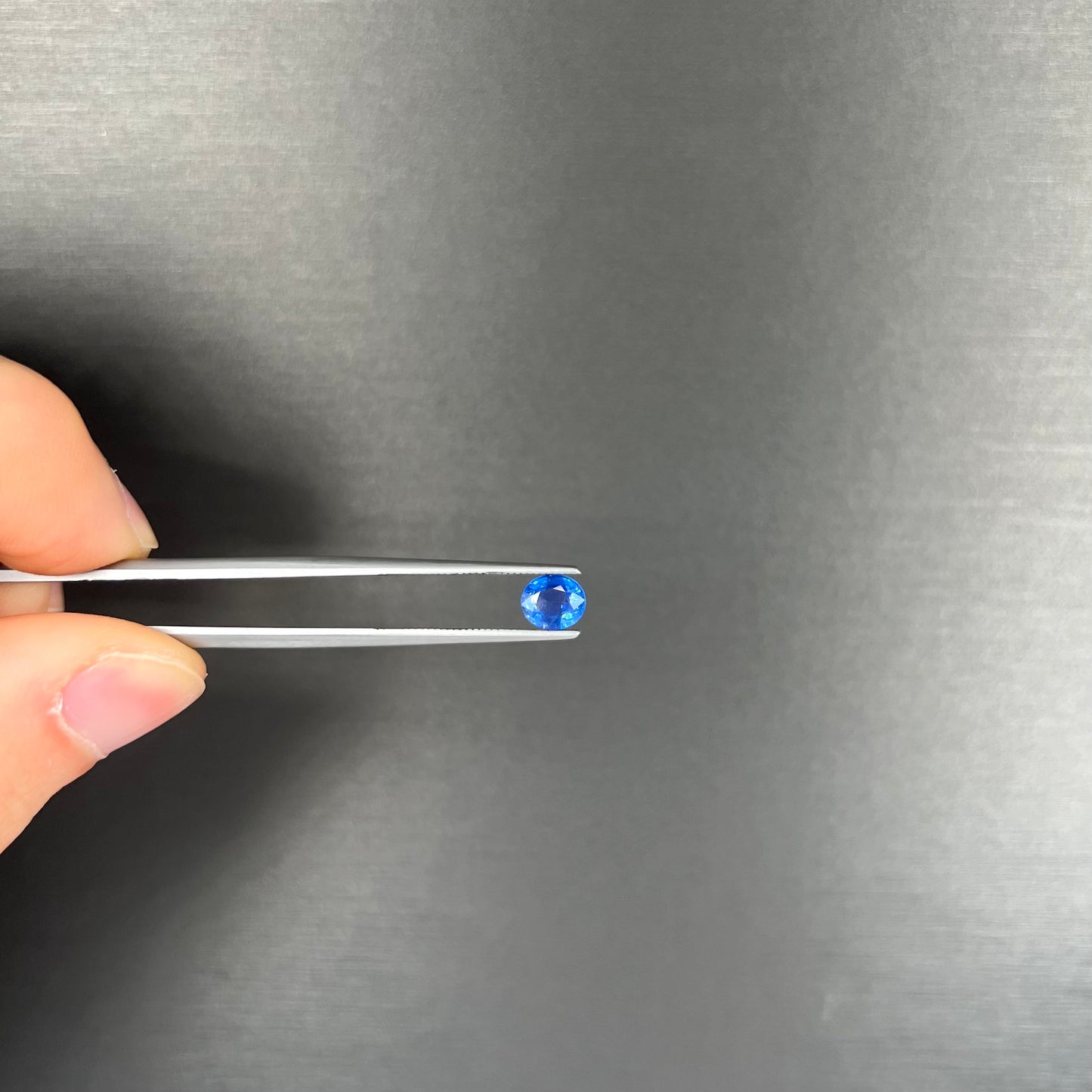 A loose, faceted oval cut natural blue sapphire. The color is a dark cornflower blue.