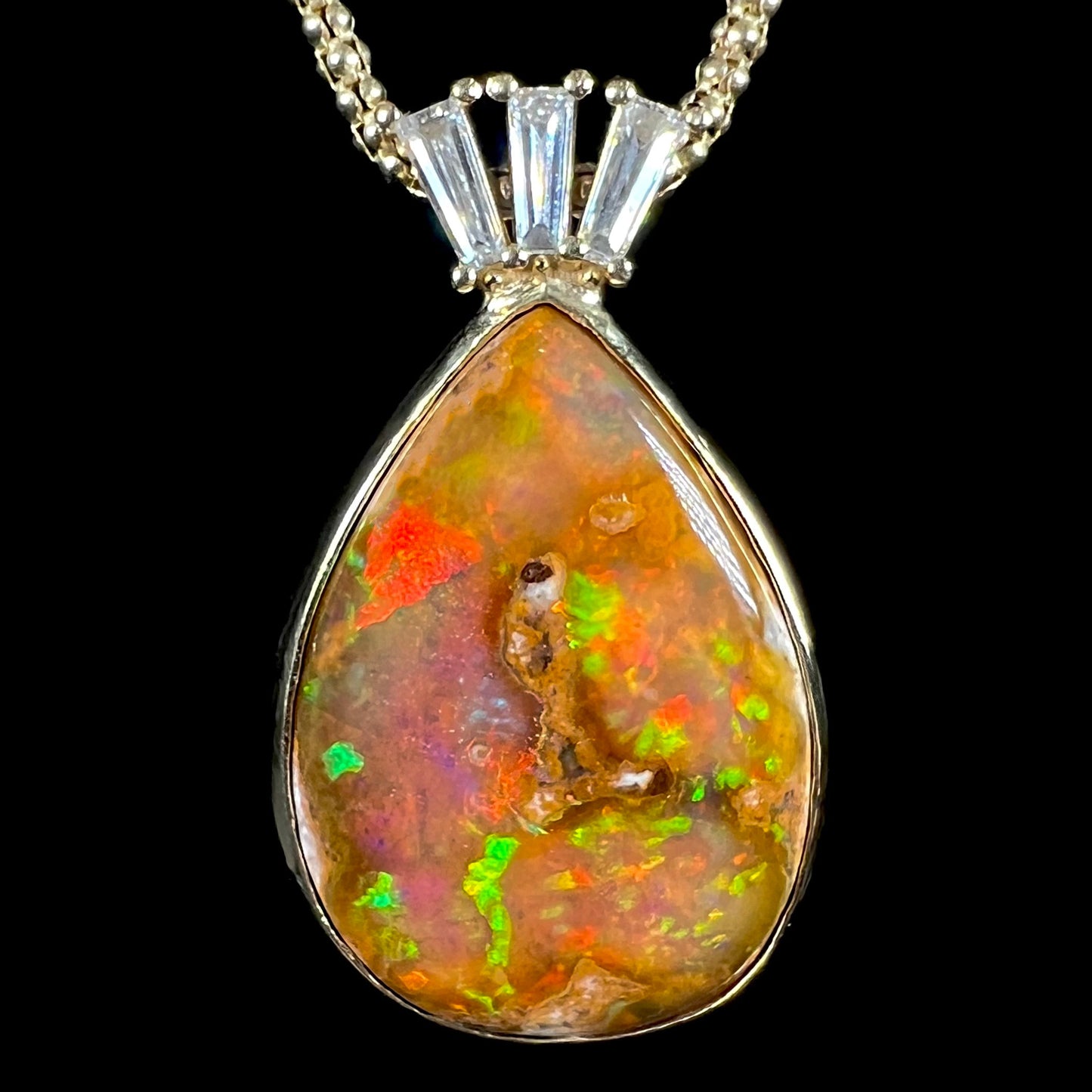 A unisex pear shaped fire opal pendant set with tapered baguette cut diamond accents in 18 karat gold.