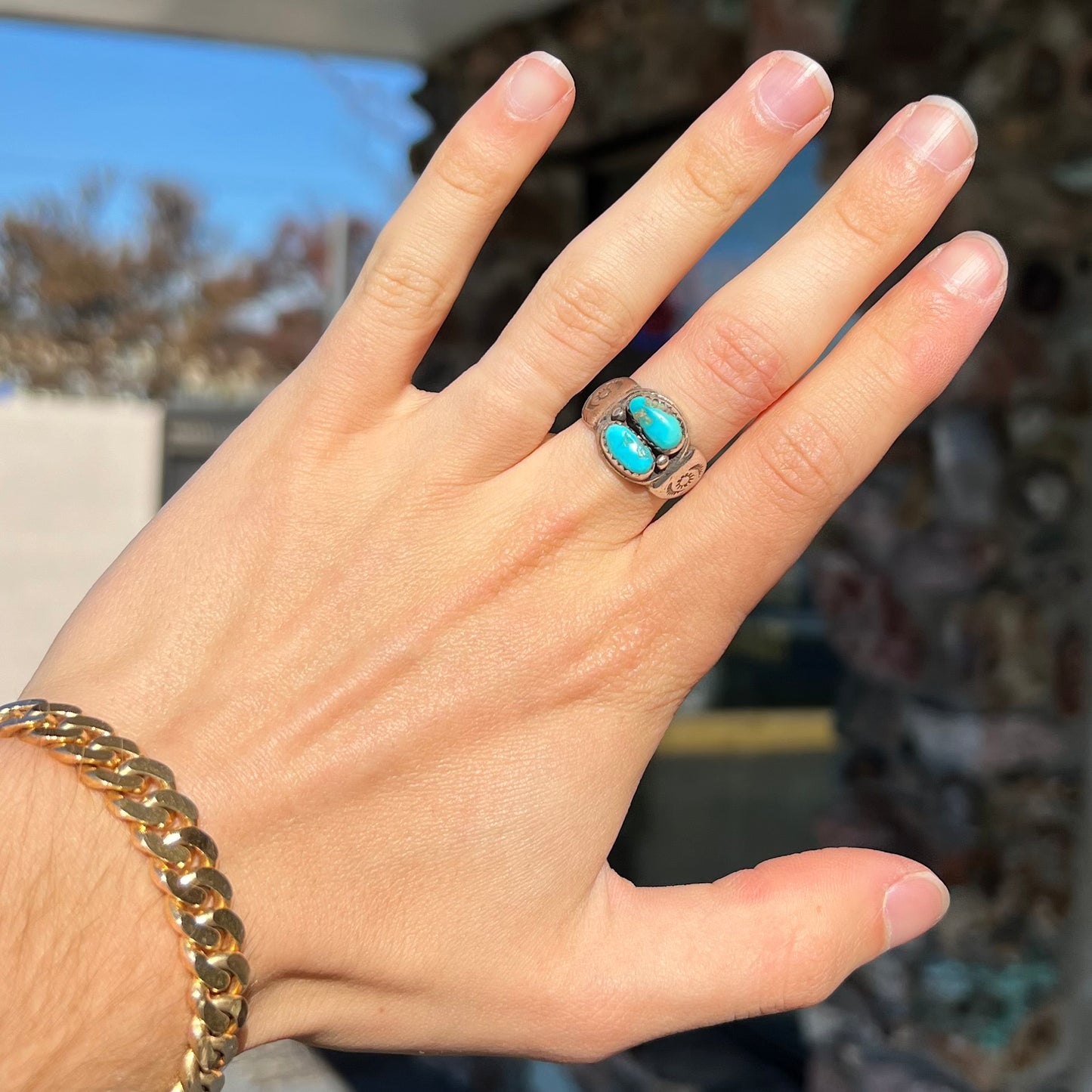 A unisex sterling silver ring bezel set with two Pilot Mountain turquoise stones. The ring is stamped with sun patterns.