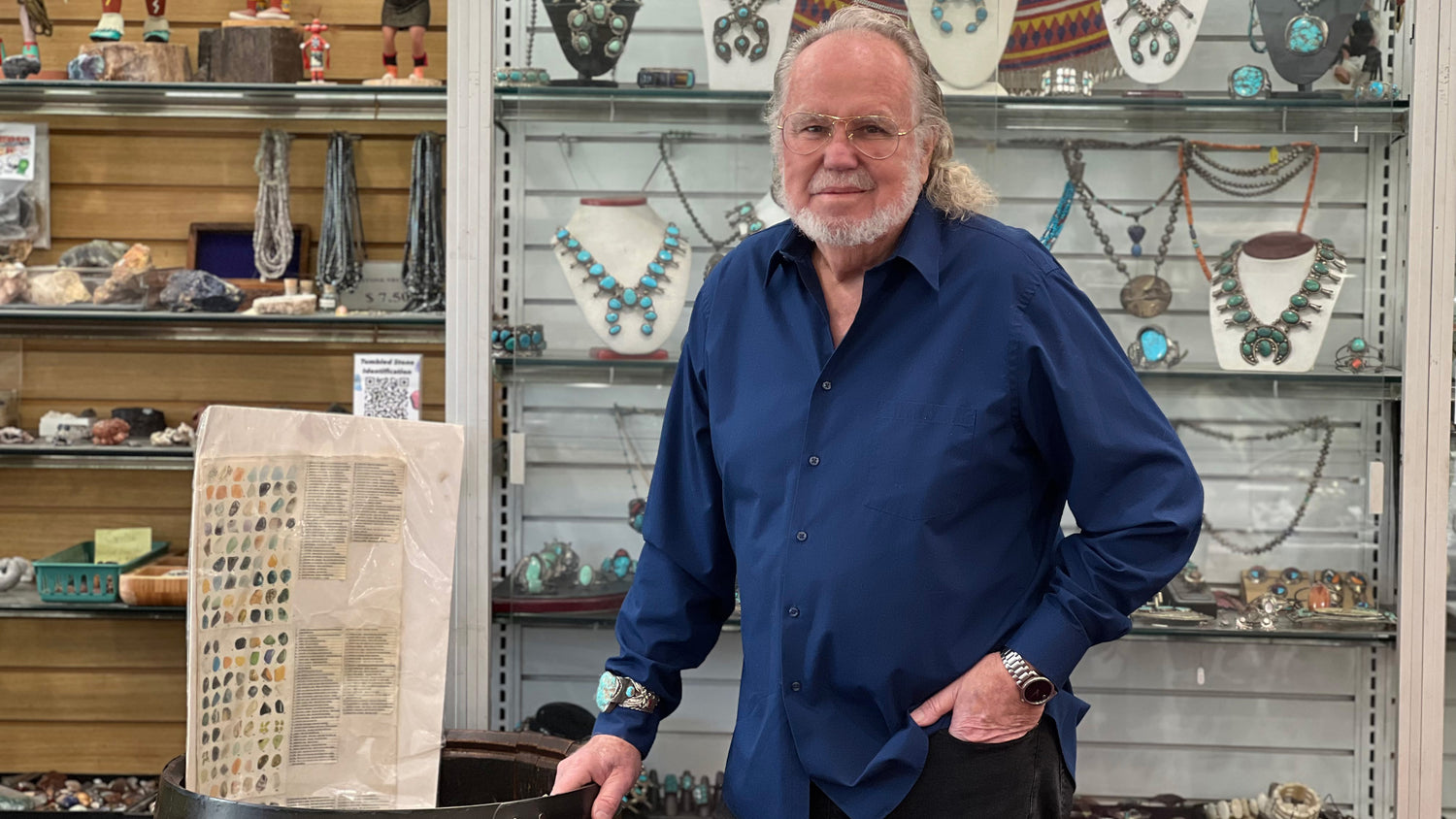 David Burton, the owner of Burton's Gems and Opals, standing in front of Native American turquoise squash blossom necklaces.