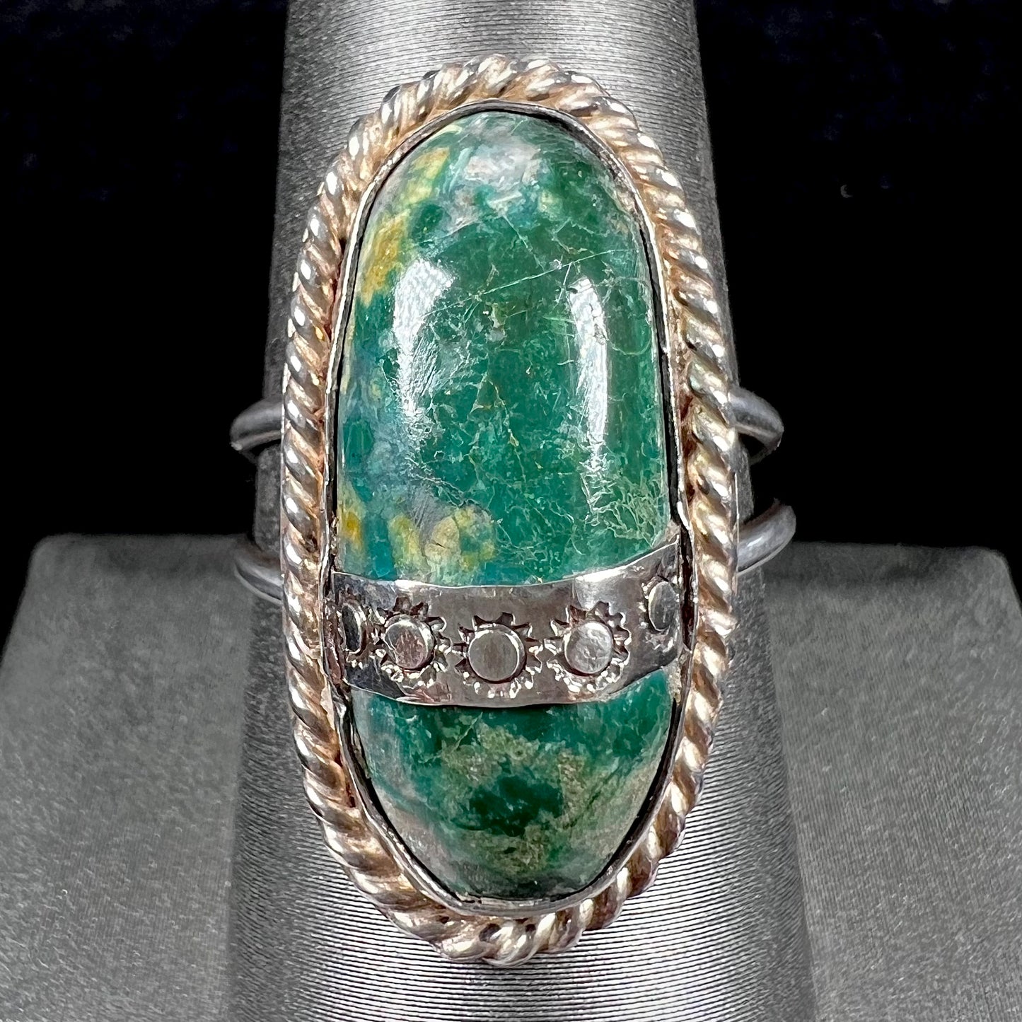 A green agate solitaire ring handmade from sterling silver. There is a stamped pattern of suns across a strip of metal over the stone.