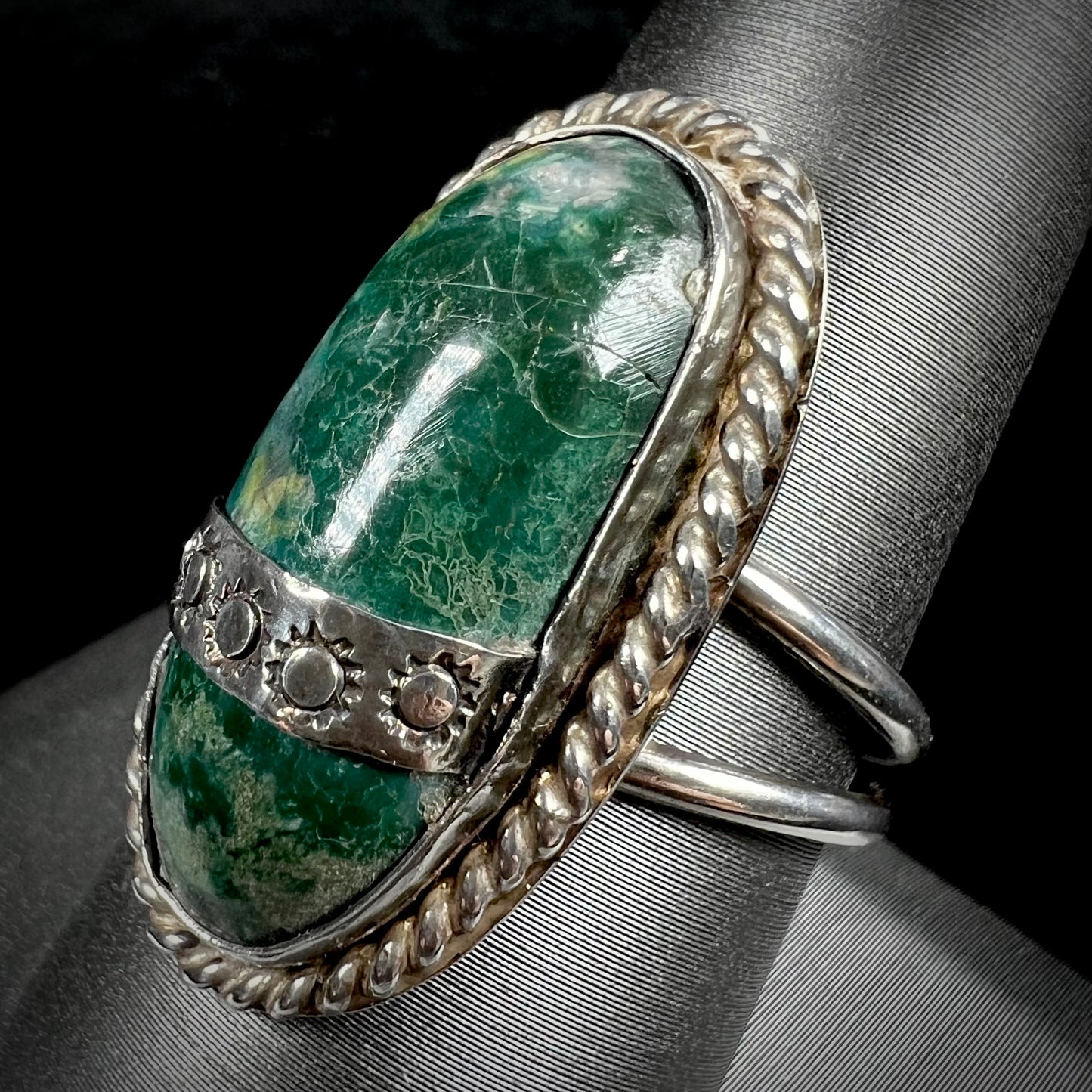 A green agate solitaire ring handmade from sterling silver. There is a stamped pattern of suns across a strip of metal over the stone.