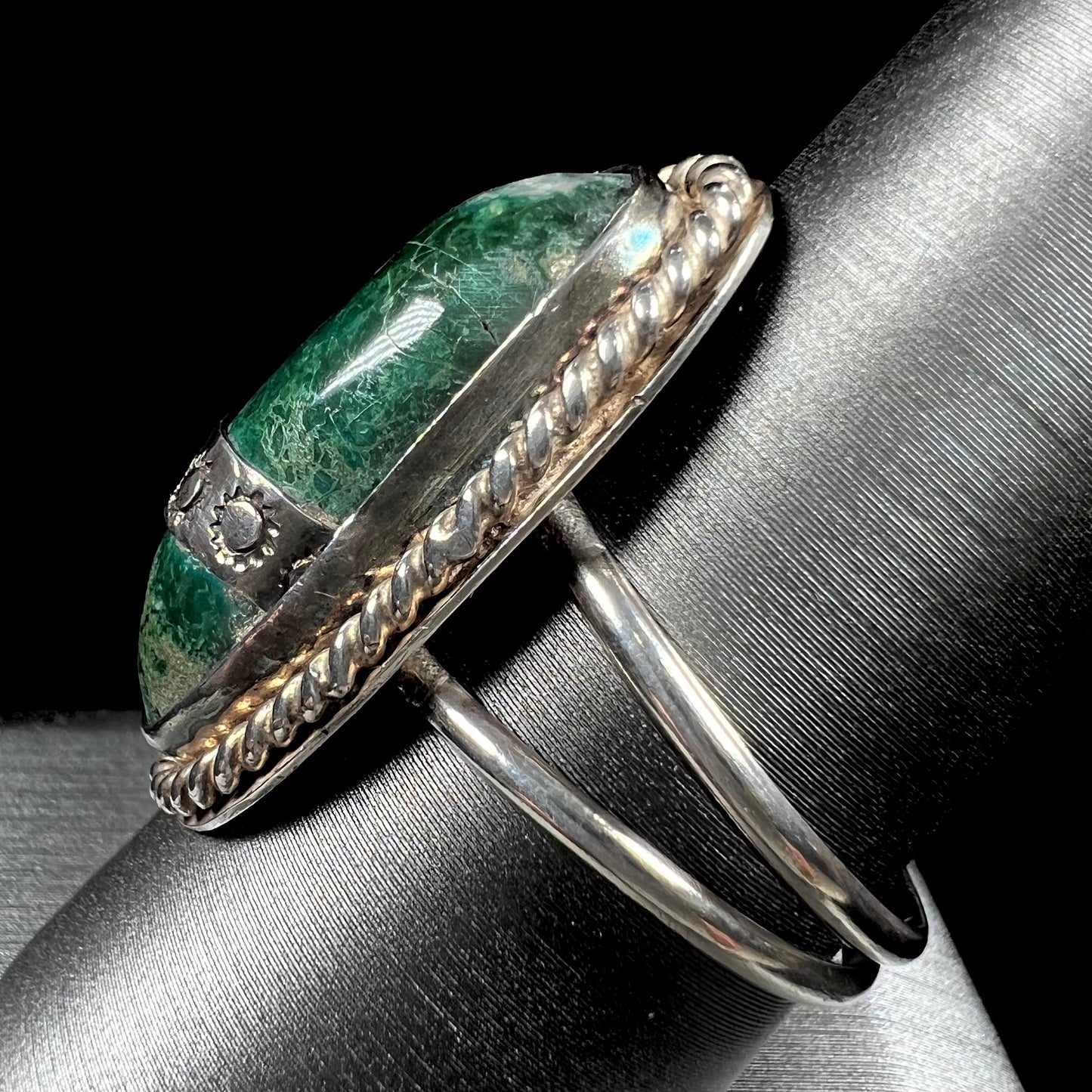 A green agate solitaire ring handmade from sterling silver. There is a stamped pattern of suns across a strip of metal over the stone.