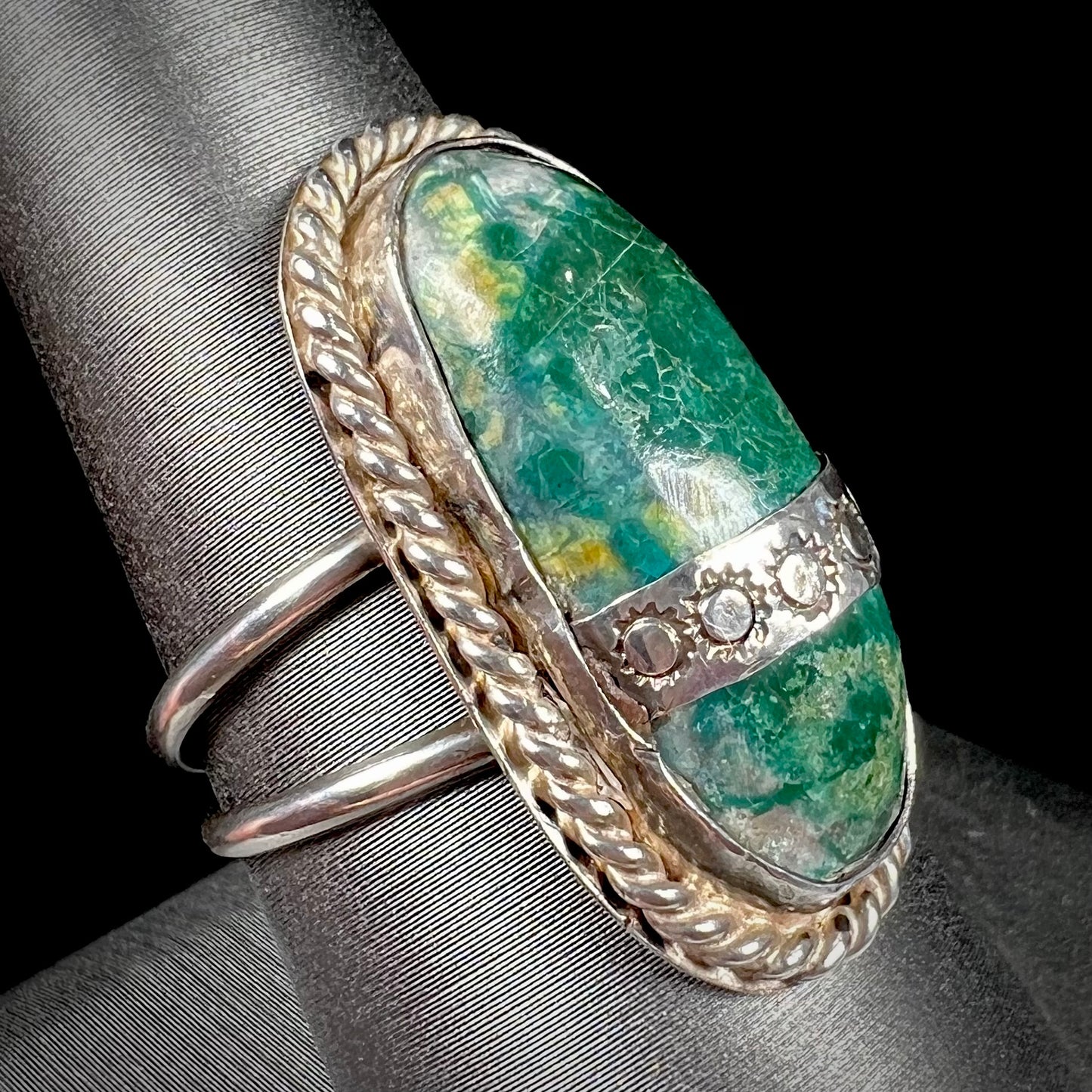 A green agate solitaire ring handmade from sterling silver. There is a stamped pattern of suns across a strip of metal over the stone.