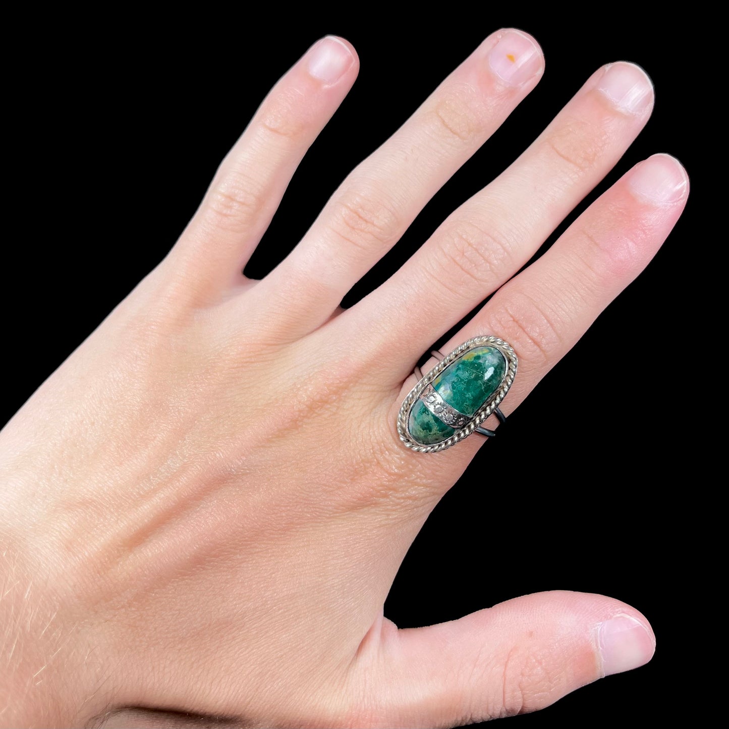 A green agate solitaire ring handmade from sterling silver. There is a stamped pattern of suns across a strip of metal over the stone.
