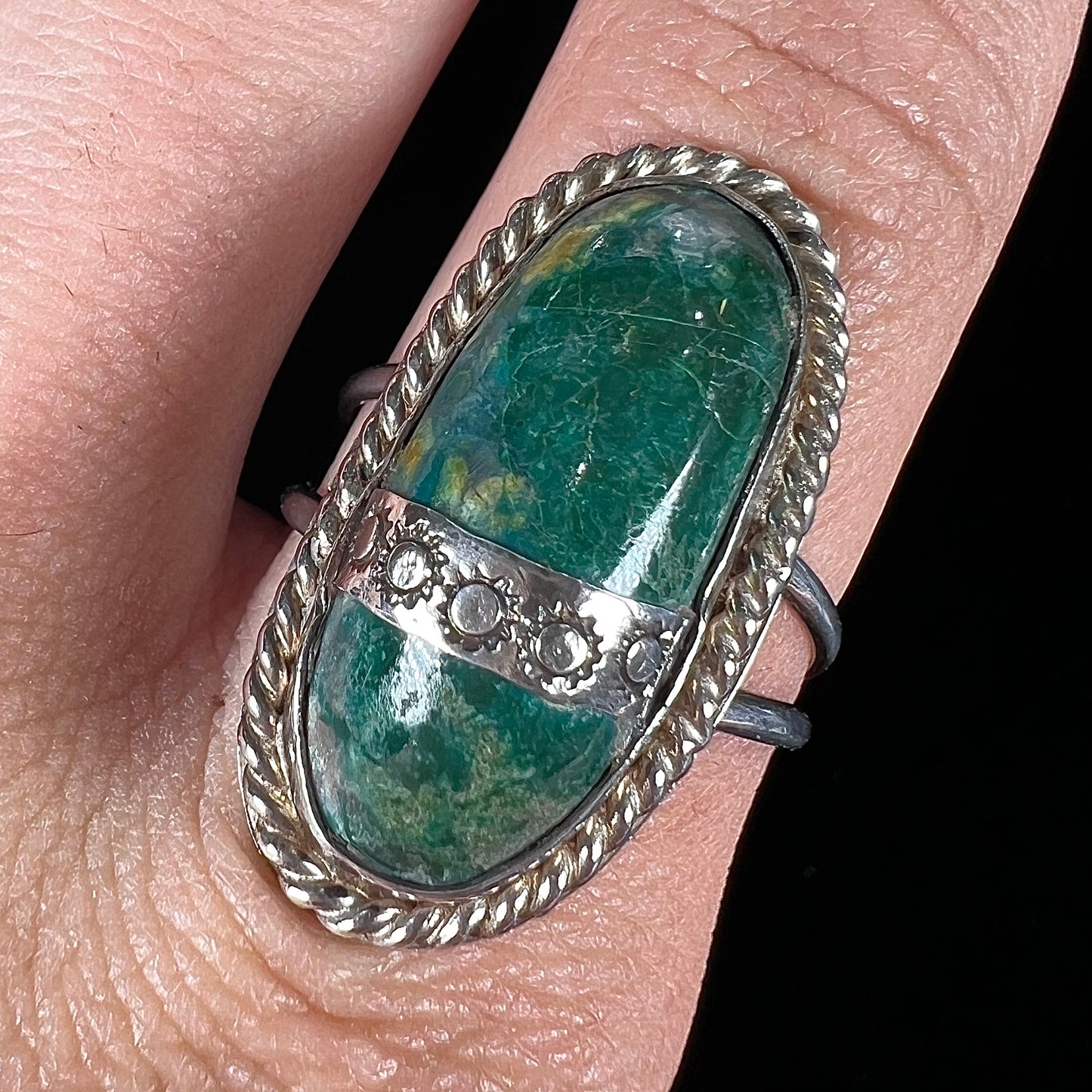 A green agate solitaire ring handmade from sterling silver. There is a stamped pattern of suns across a strip of metal over the stone.