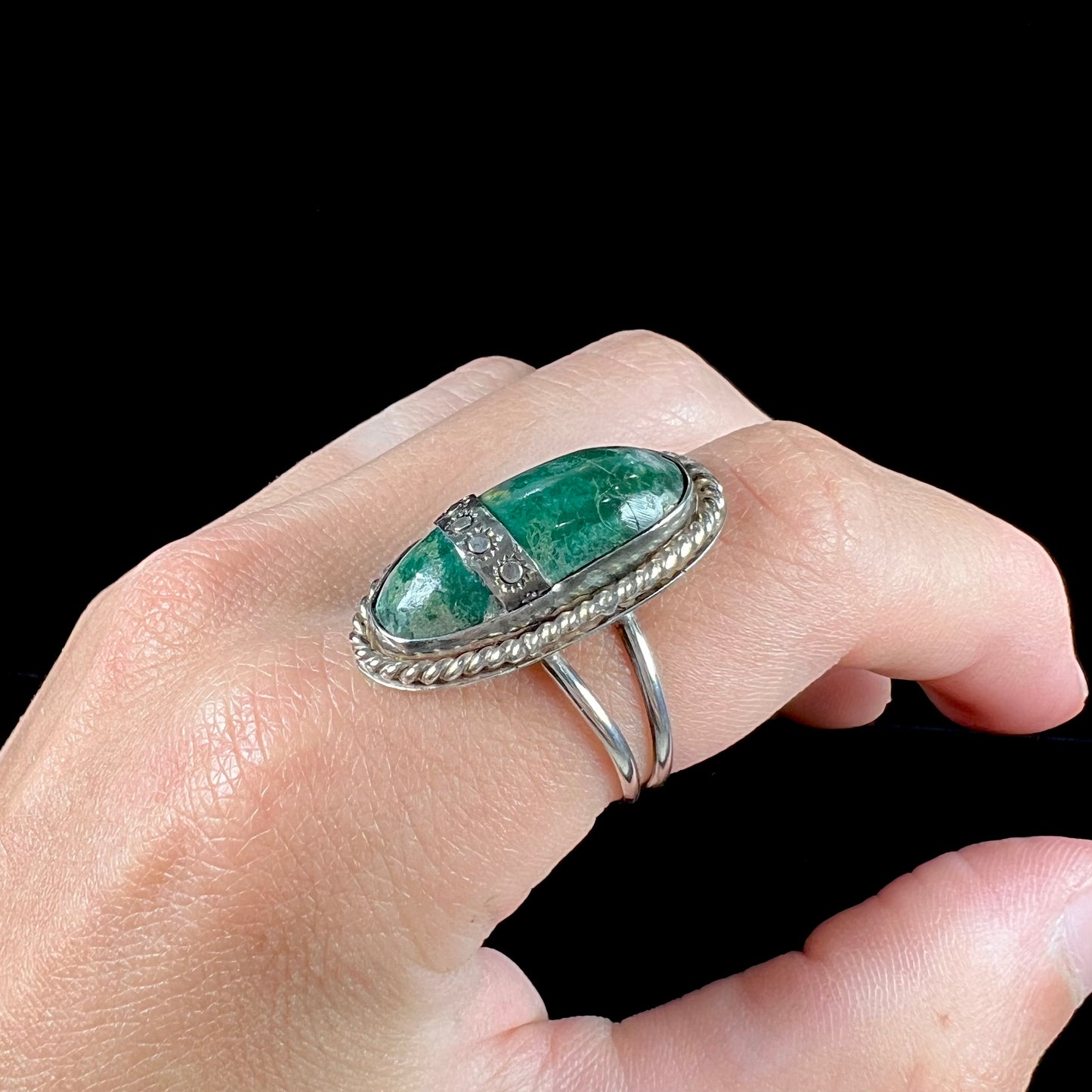 A green agate solitaire ring handmade from sterling silver. There is a stamped pattern of suns across a strip of metal over the stone.