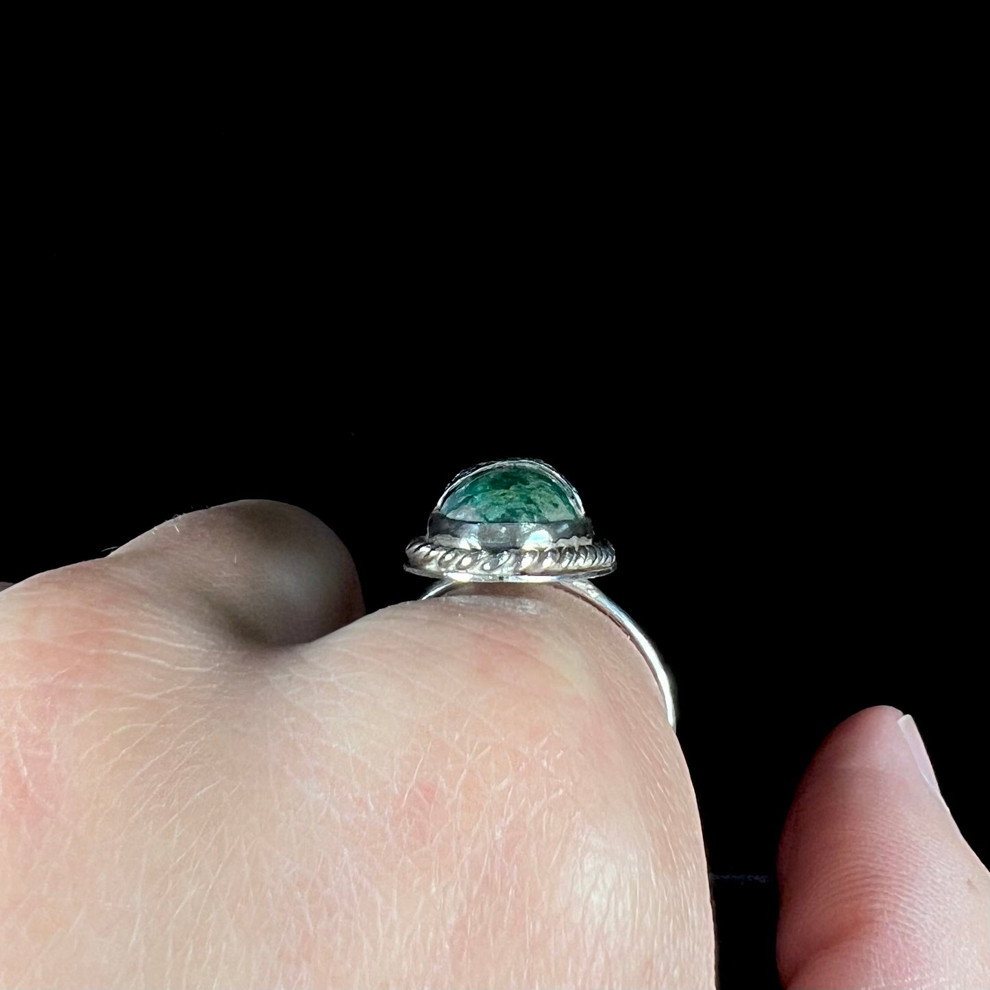 A green agate solitaire ring handmade from sterling silver. There is a stamped pattern of suns across a strip of metal over the stone.