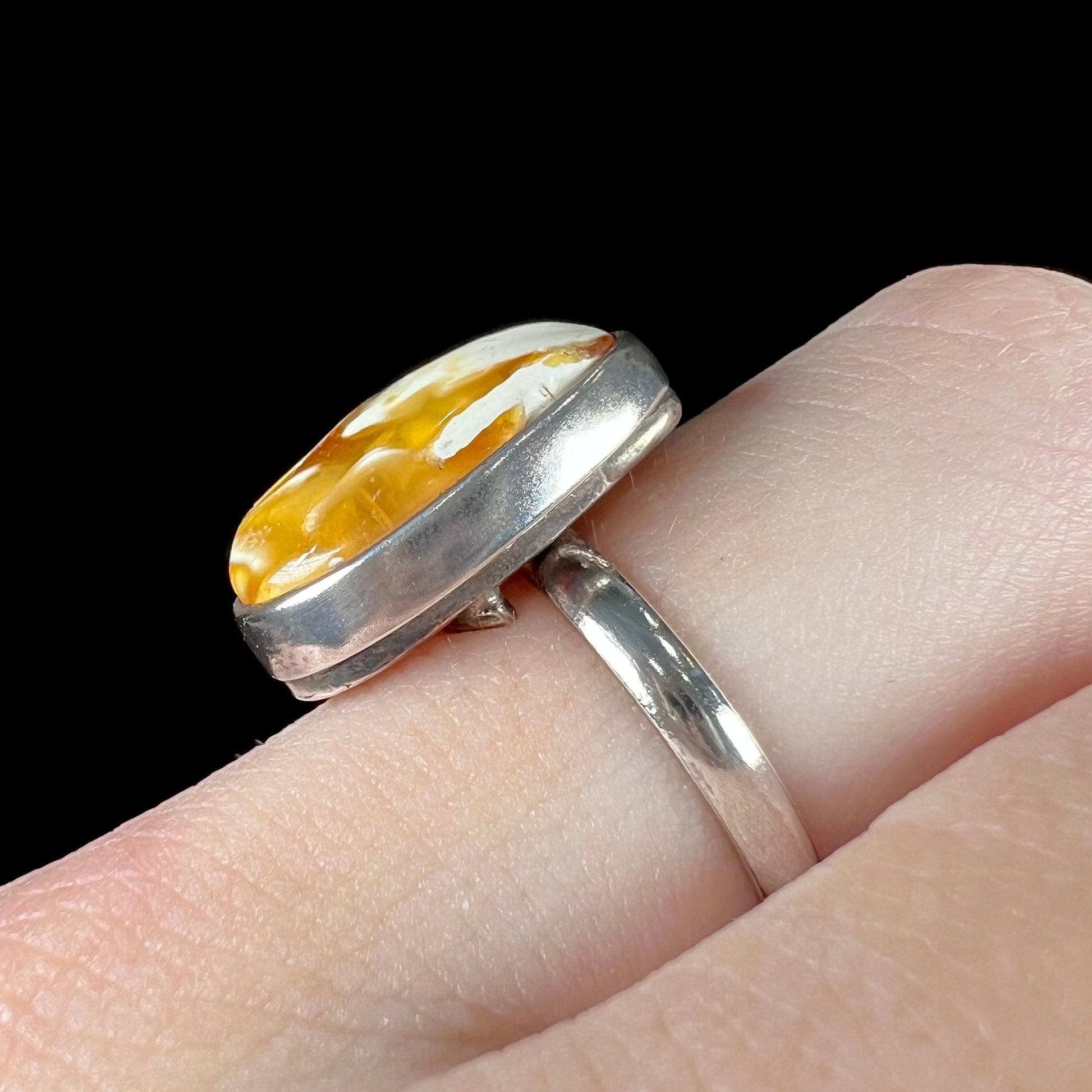 An adjustable sterling silver solitaire ring set with a cabochon cut butterscotch amber stone.