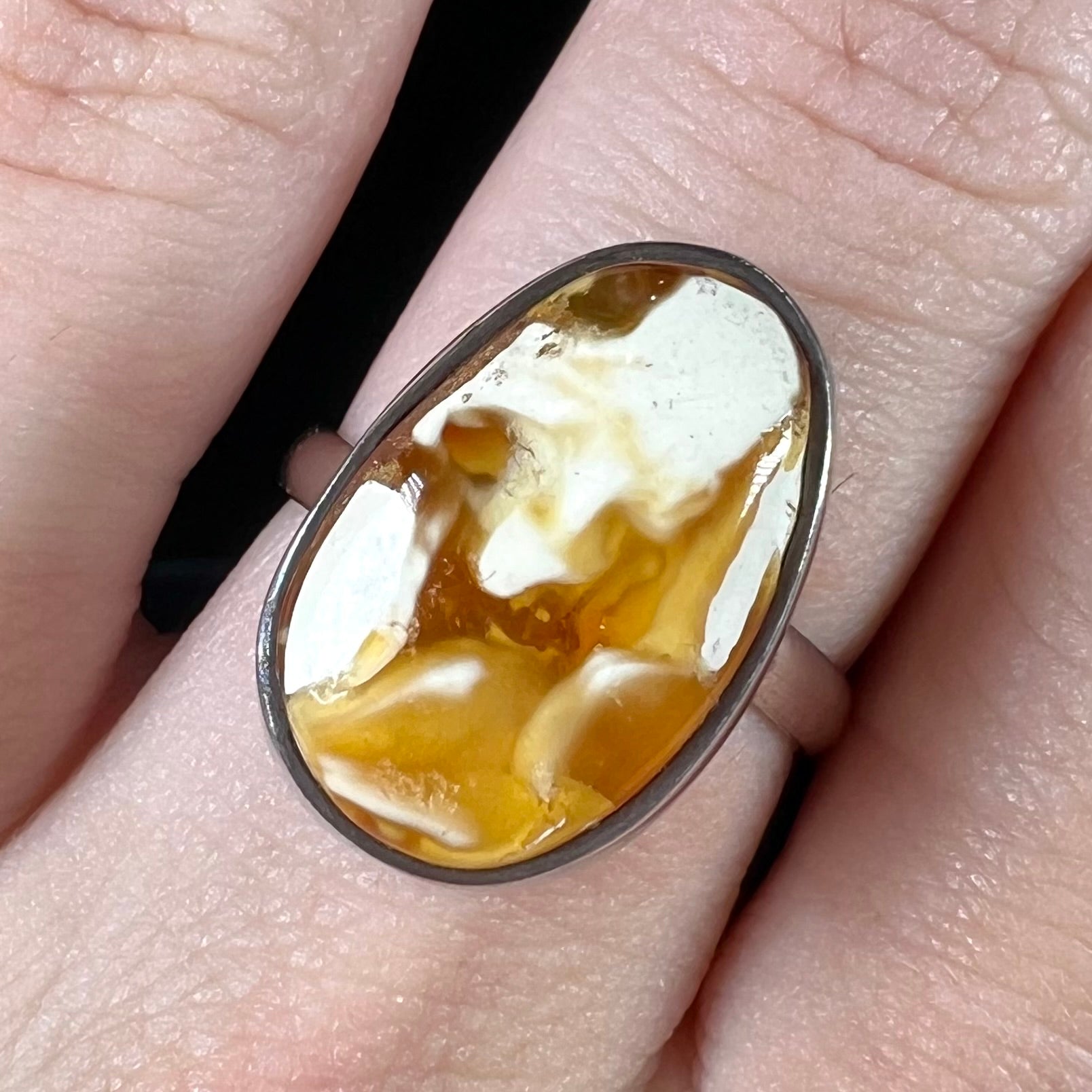 An adjustable sterling silver solitaire ring set with a cabochon cut butterscotch amber stone.