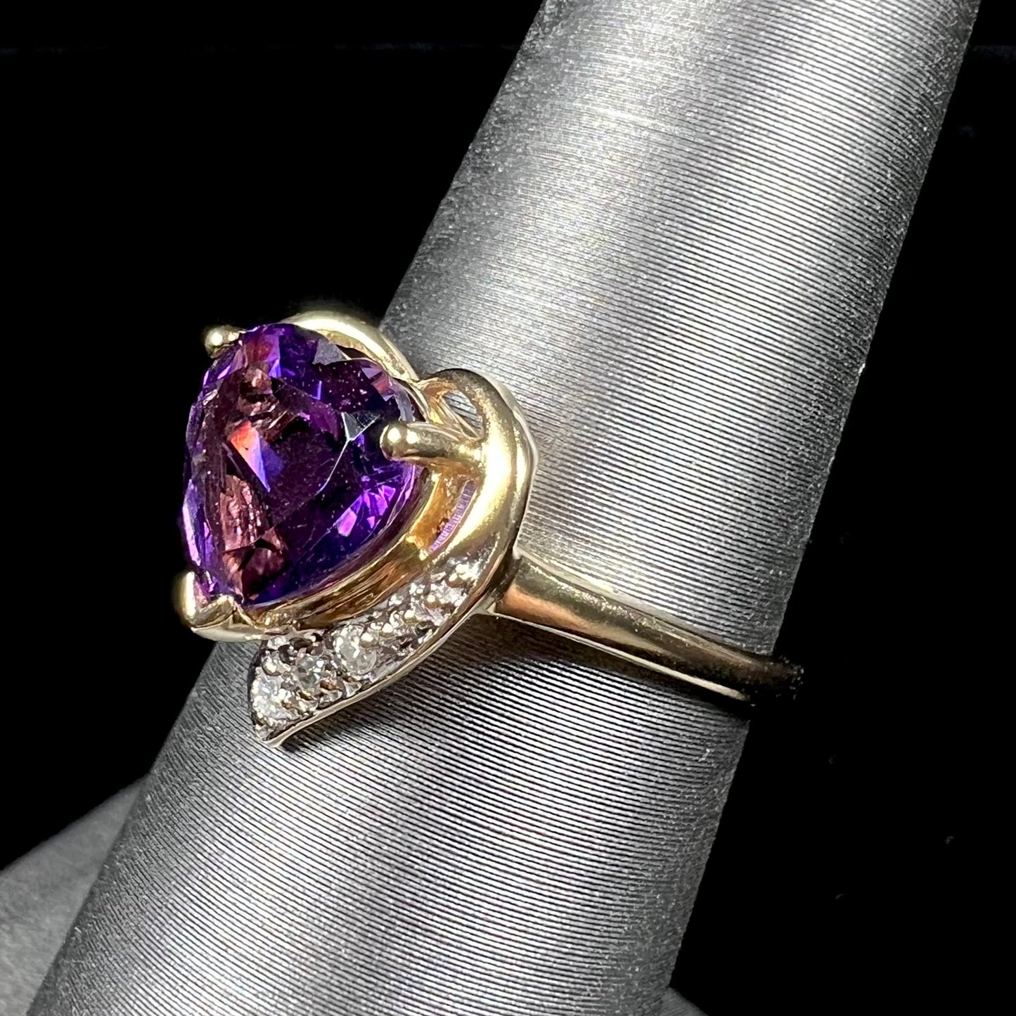 A ladies' yellow gold ring set with a heart shaped amethyst and round cut diamond accents.