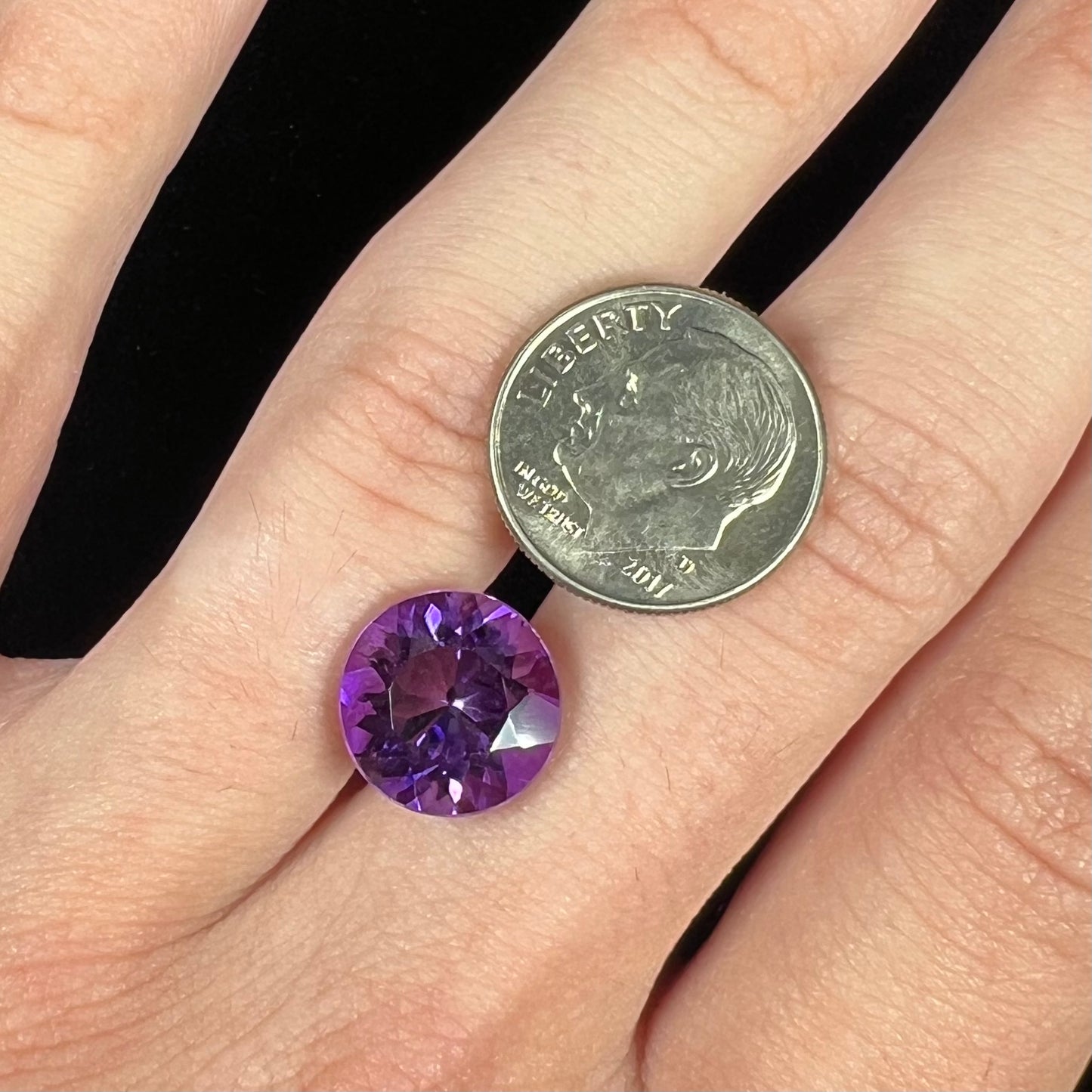 A loose, faceted round brilliant cut amethyst gemstone.  The stone is purple with blue flashes.