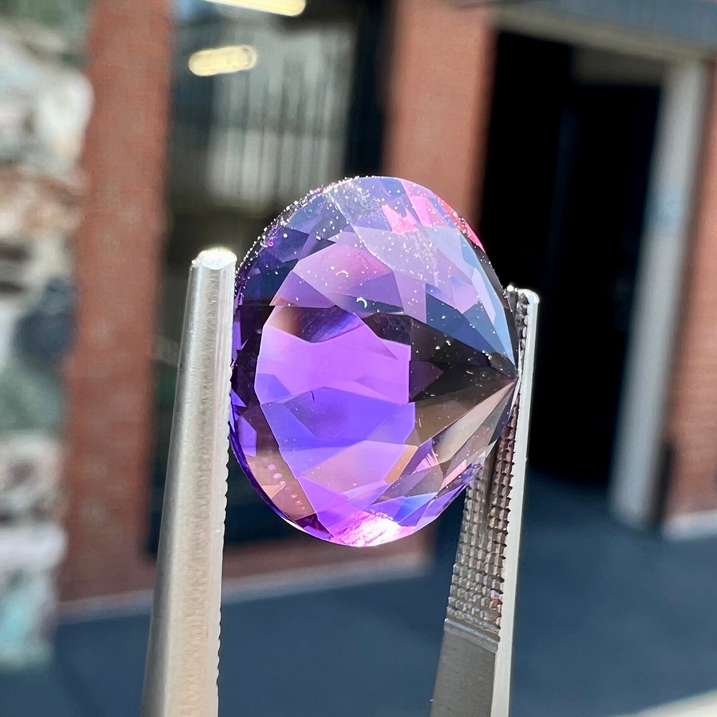 A loose, faceted round brilliant cut amethyst gemstone. The stone is purple with blue flashes.