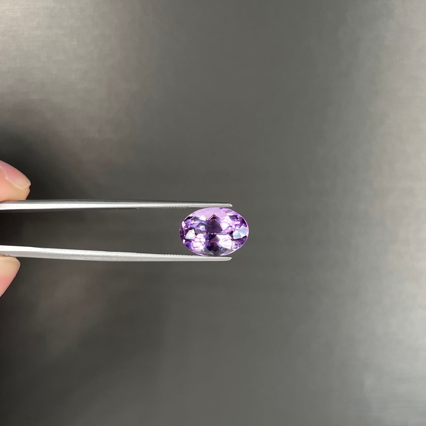A faceted oval cut amethyst gemstone. The stone is a light purple color.
