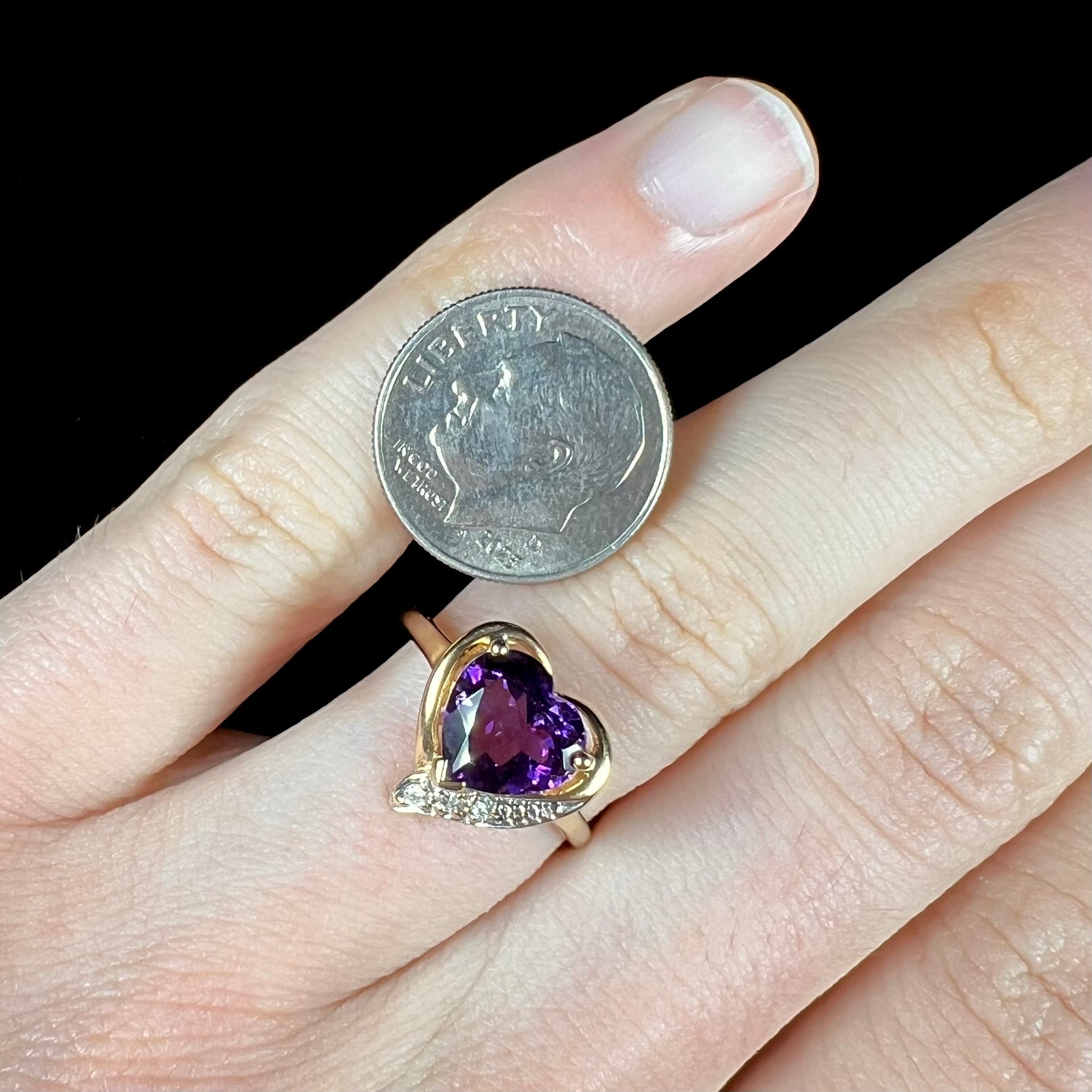 A ladies' yellow gold ring set with a heart shaped amethyst and round cut diamond accents.