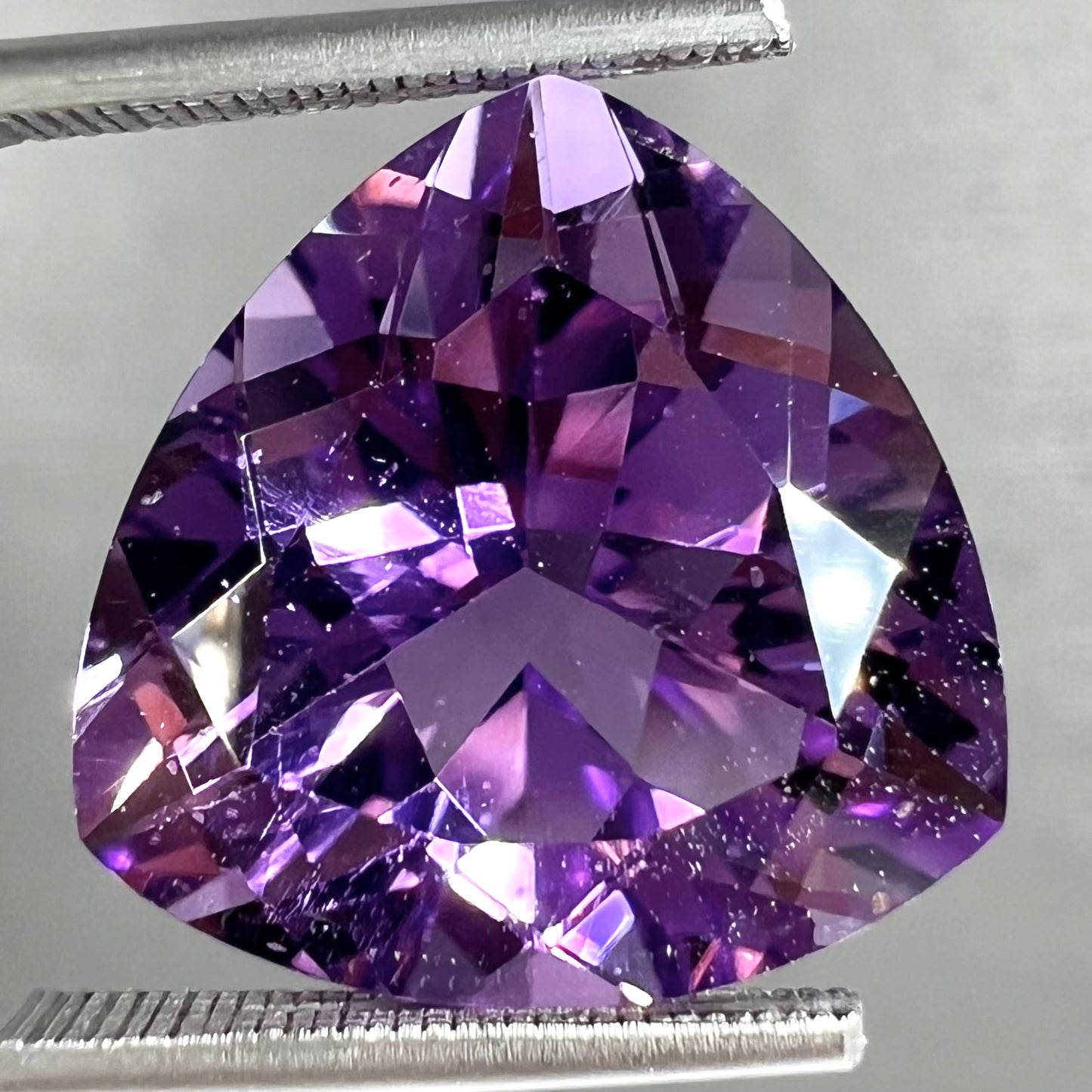A loose, faceted trillion cut amethyst gemstone.