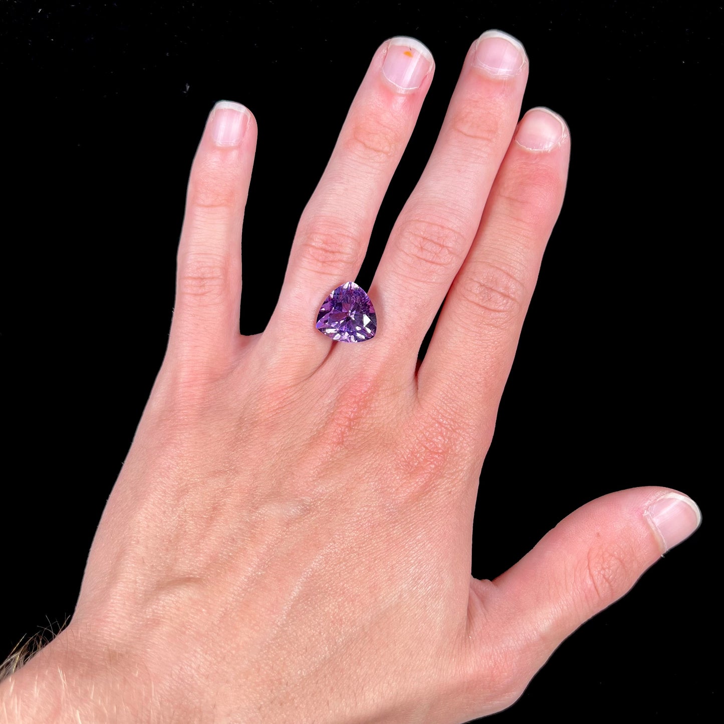 A loose, faceted trillion cut amethyst gemstone.