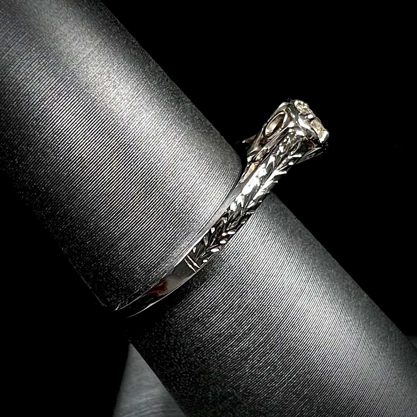 An Art Deco style 18 karat white gold diamond solitaire ring. The ring has scroll work on the side of the shank.