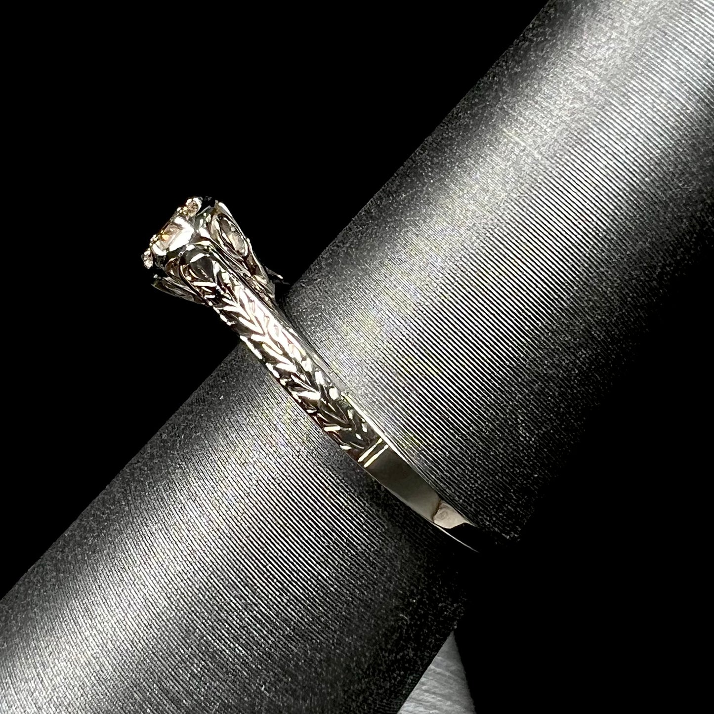 An Art Deco style 18 karat white gold diamond solitaire ring. The ring has scroll work on the side of the shank.