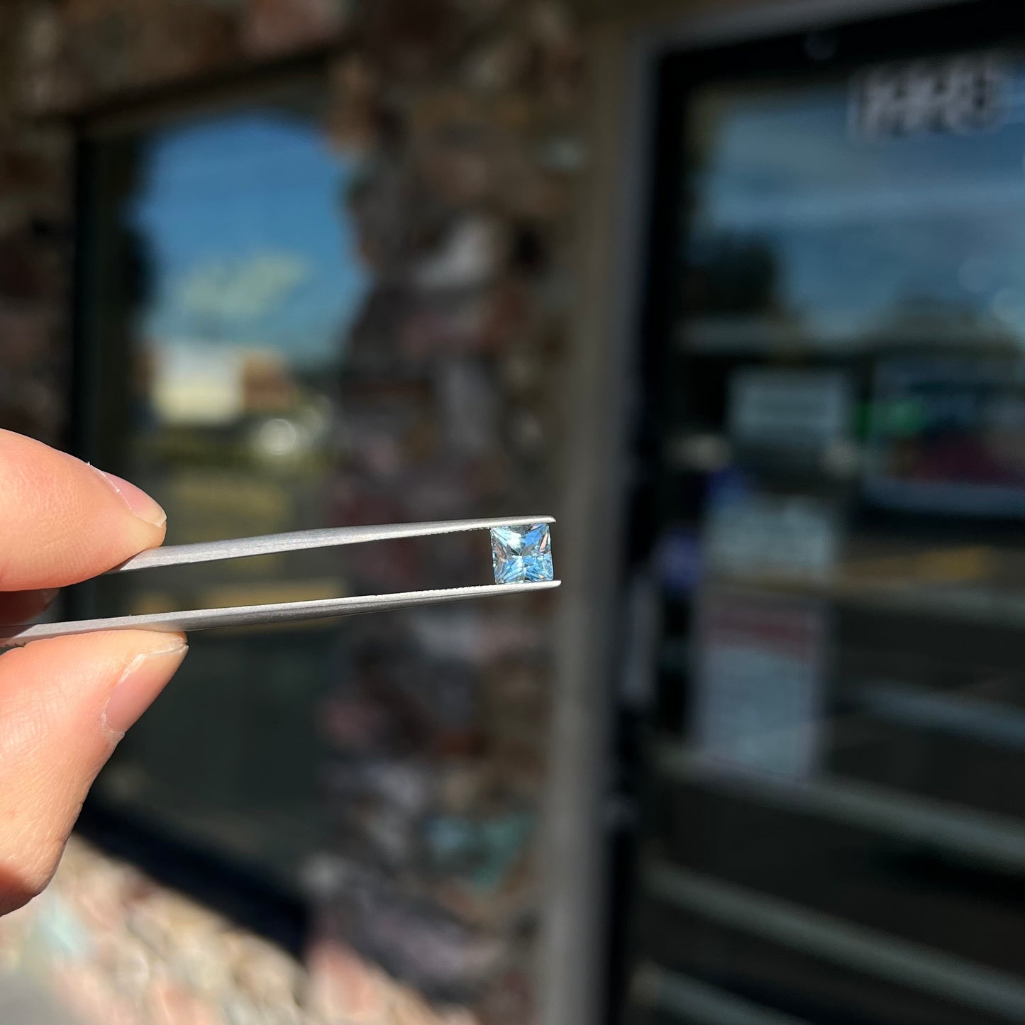 A loose, princess cut aquamarine gemstone. The stone is a light blue color.