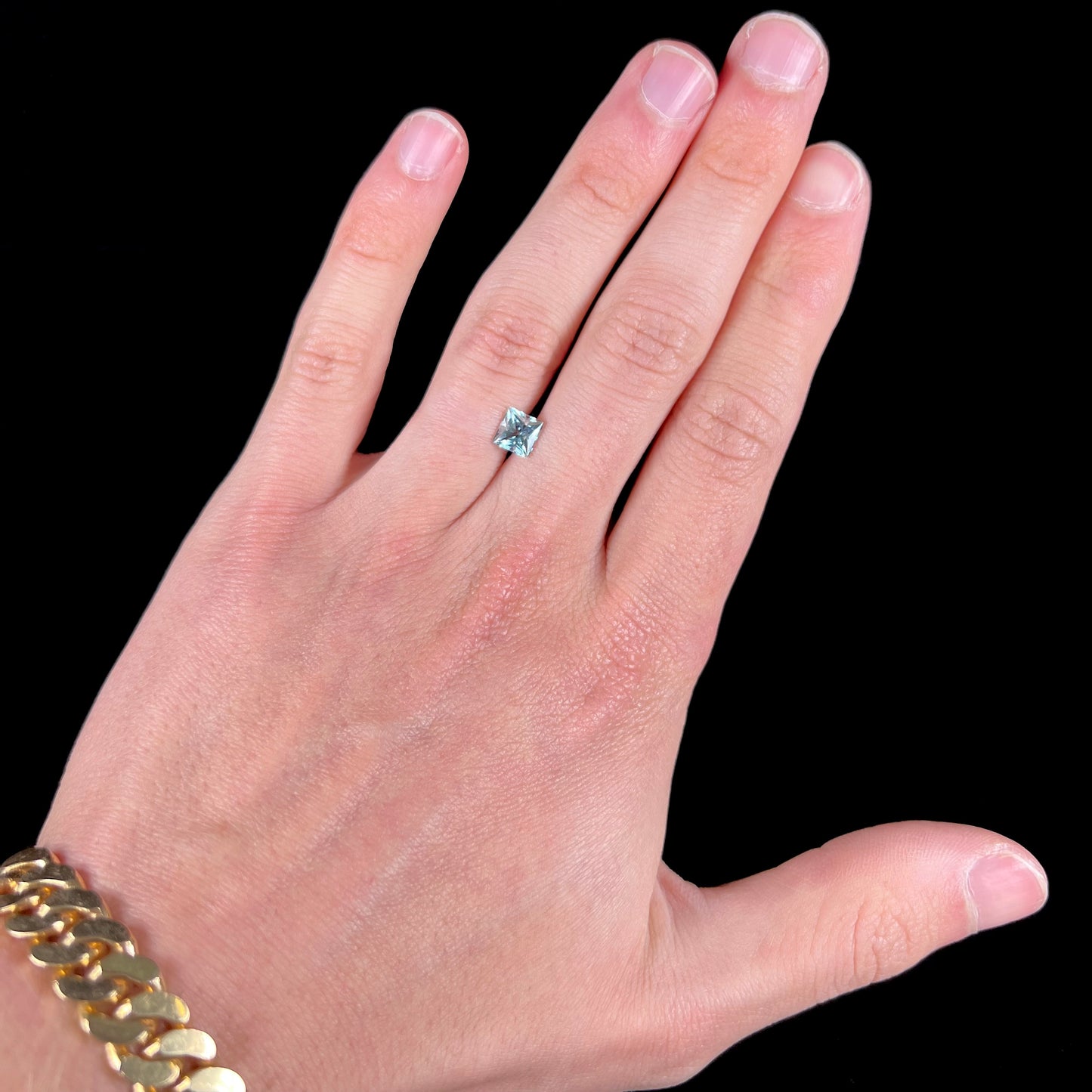 A loose, princess cut aquamarine gemstone. The stone is a light blue color.