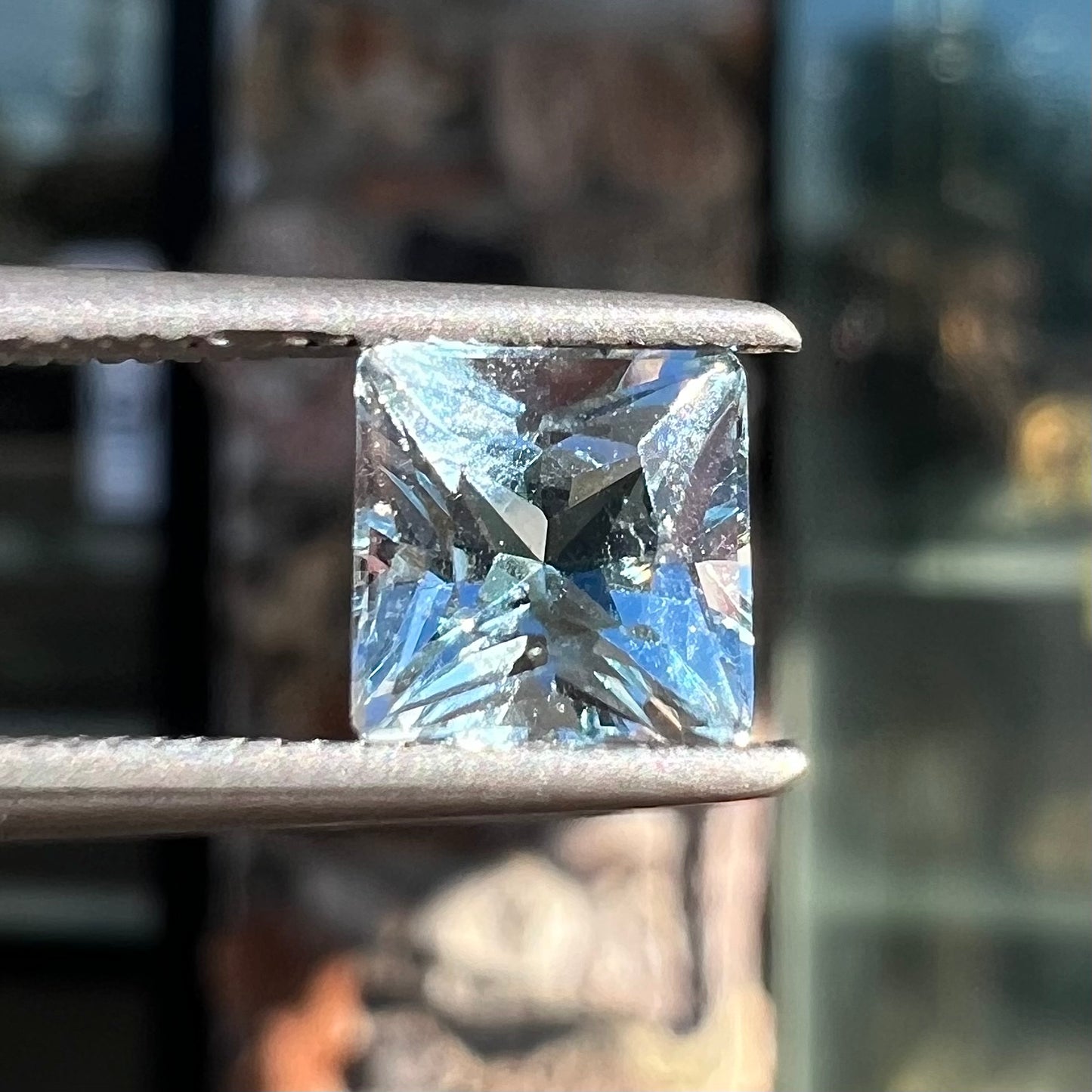 A loose, princess cut aquamarine gemstone. The stone is a light blue color.