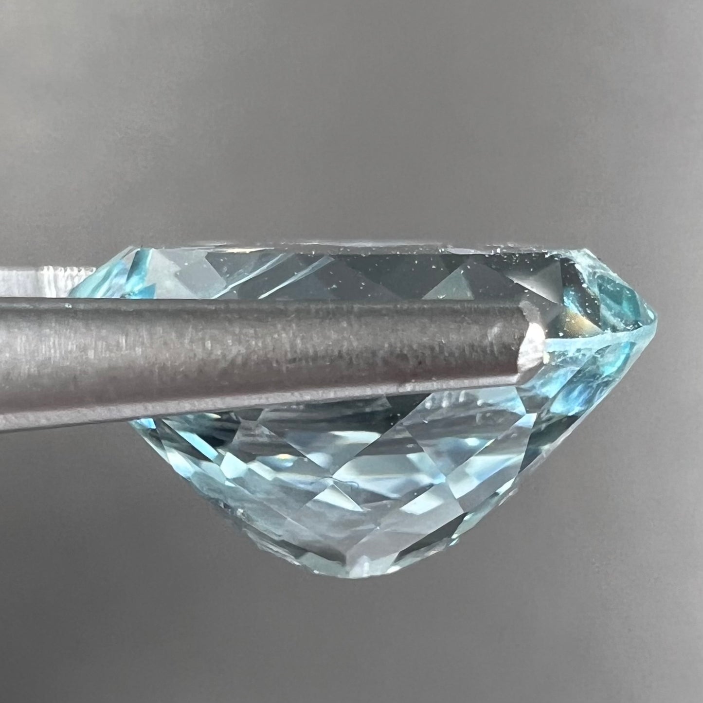 A loose, faceted oval cut aquamarine gemstone from Brazil. The stone is greenish blue color.