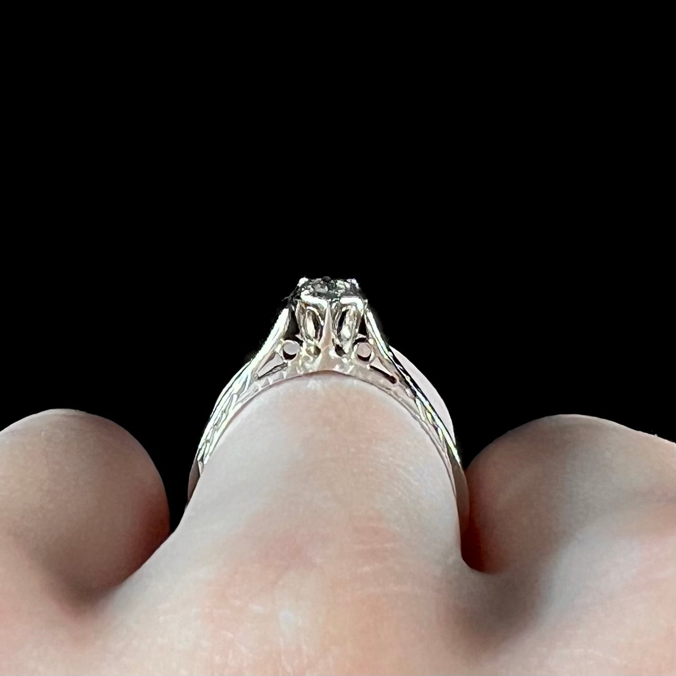 An Art Deco style 18 karat white gold diamond solitaire ring. The ring has scroll work on the side of the shank.