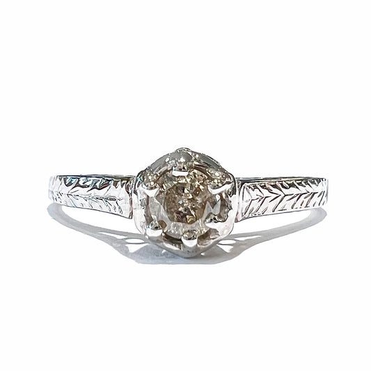 An Art Deco style 18 karat white gold diamond solitaire ring.  The ring has scroll work on the side of the shank.