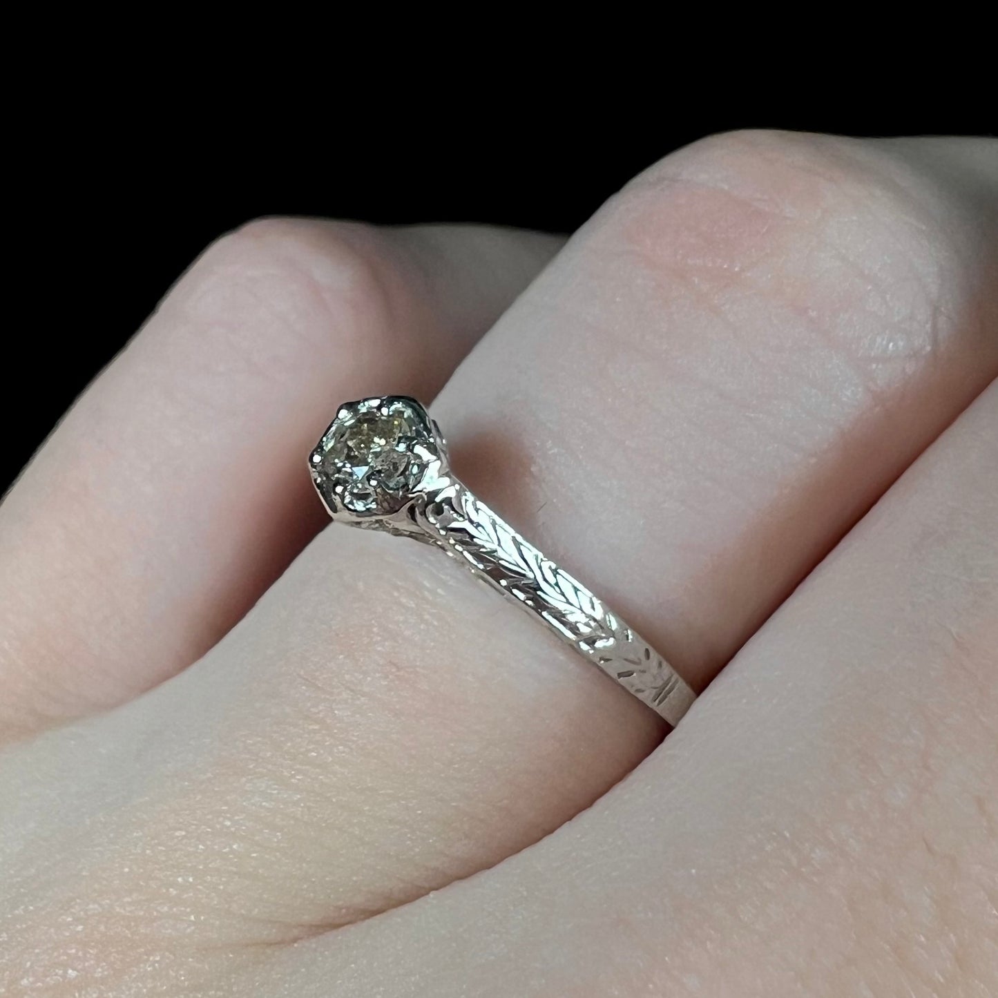 An Art Deco style 18 karat white gold diamond solitaire ring. The ring has scroll work on the side of the shank.