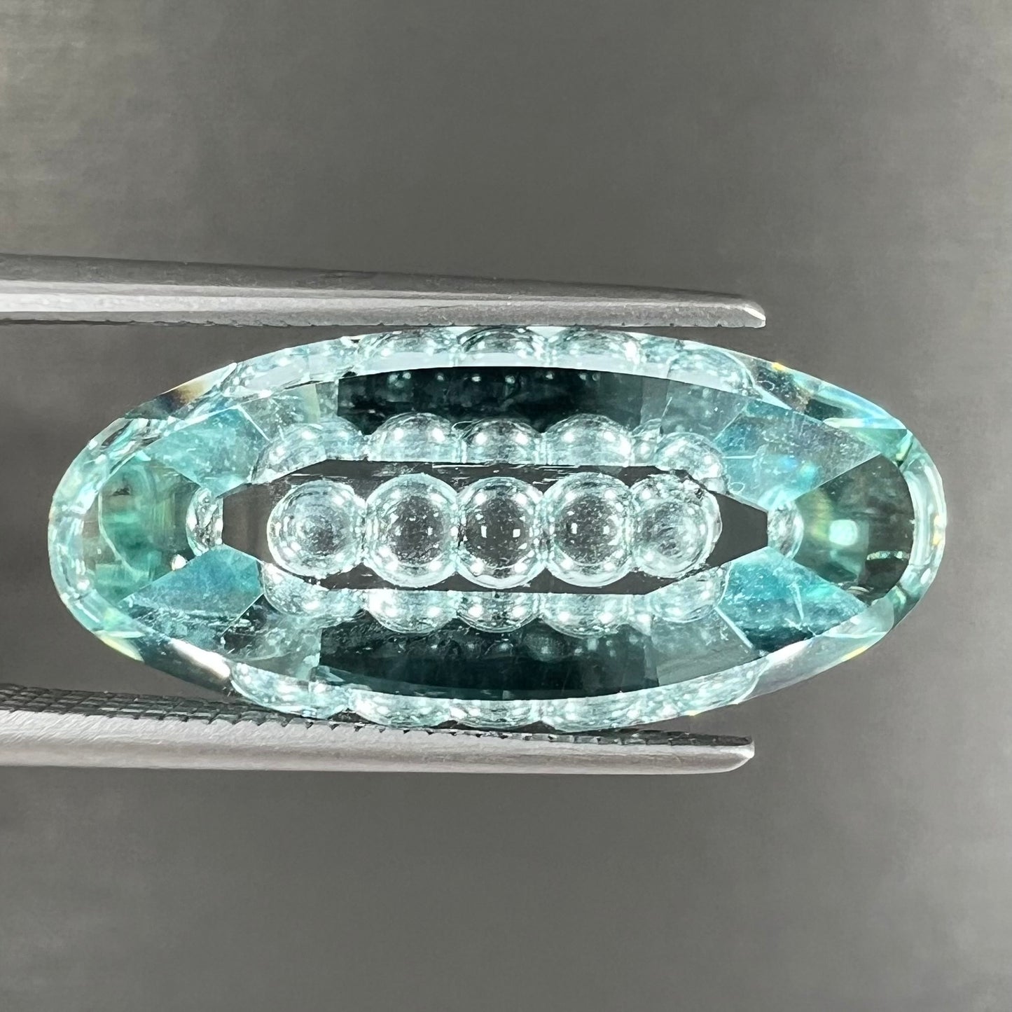 An oval fantasy cut greenish blue aquamarine stone cut by gem carver, Arthur Lee Anderson.