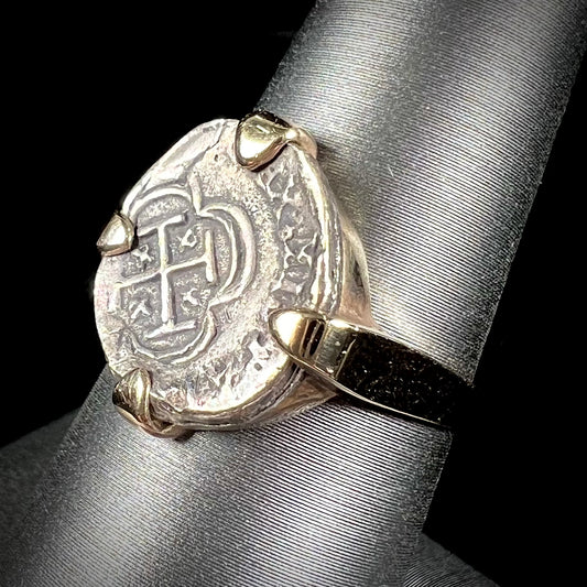 A silver Atocha 1 reale coin replica set in a yellow gold ring.