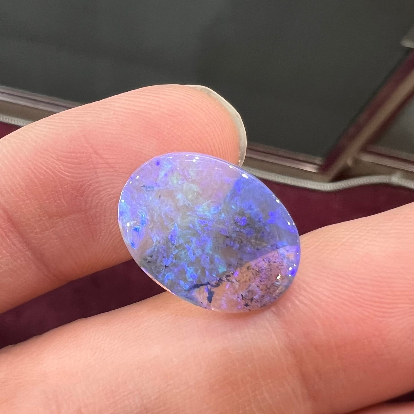 A loose, oval cabochon cut crystal opal from Lightning Ridge, Austalia that weighs 5.16 carats. The stone has blue and purple colors.