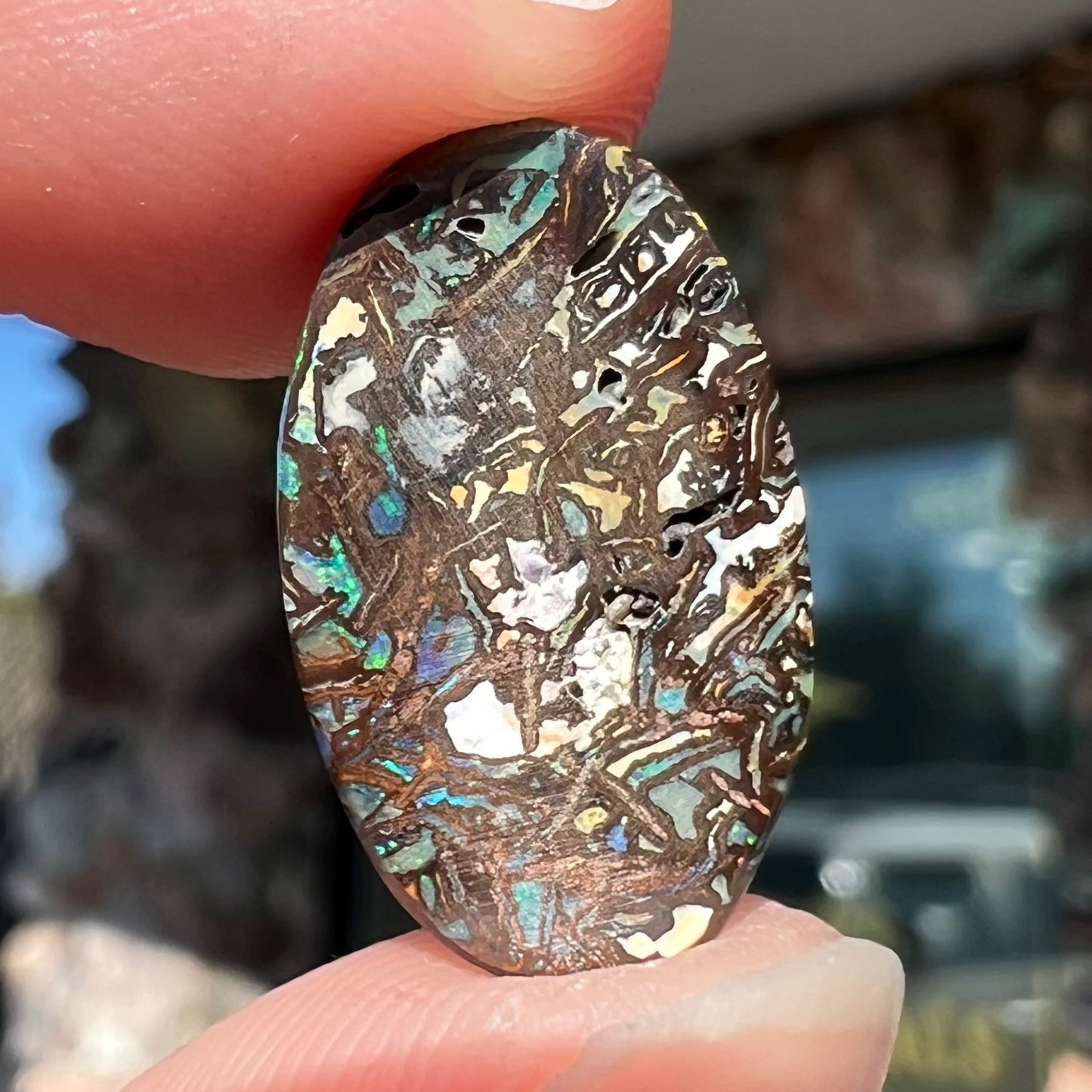 A loose, oval cabochon cut Koroit boulder opal stone. The opal has green and blue veins.