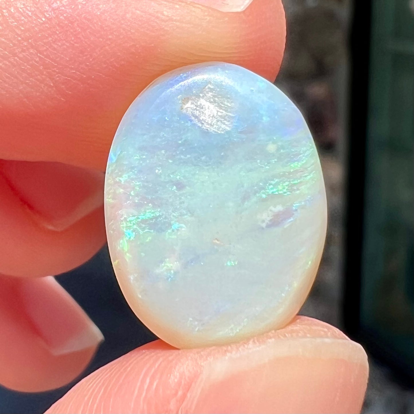 An oval cabochon cut white opal stone from Coober Pedy, Australia. The opal has subtle colors of green and blue.