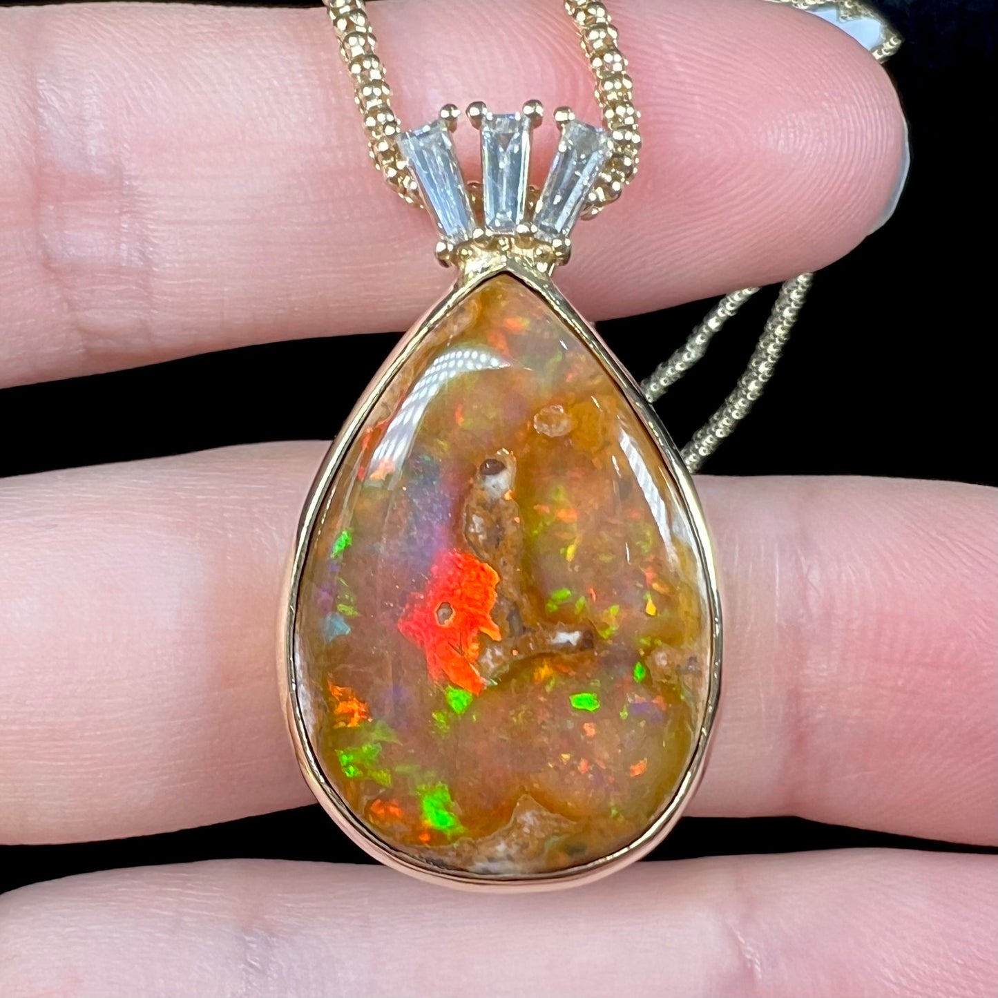 A unisex pear shaped fire opal pendant set with tapered baguette cut diamond accents in 18 karat gold.