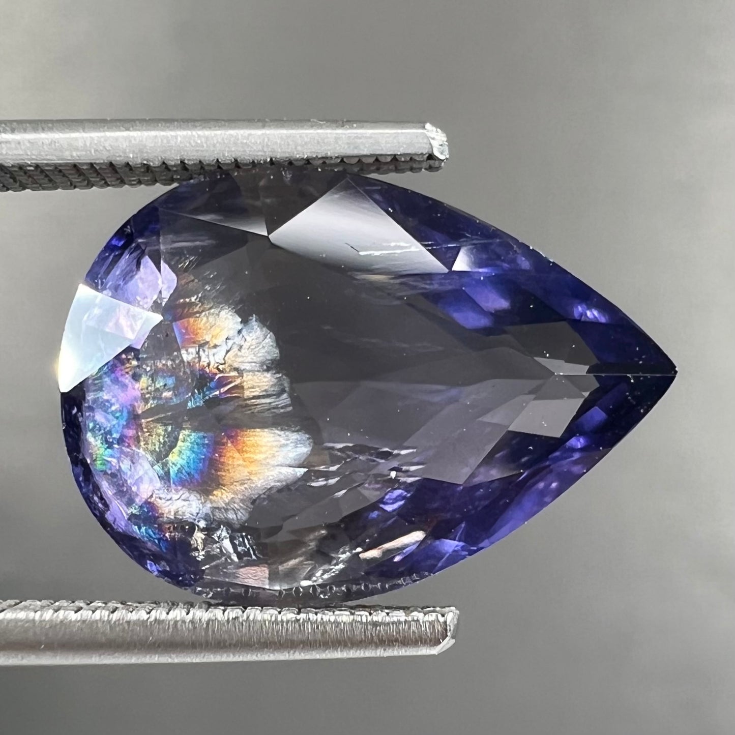 A loose, pear shaped bicolor iolite gemstone. The stone shows violite purple and silver colors.