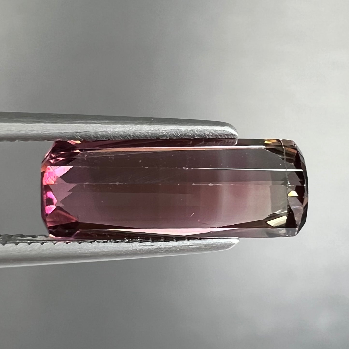 A loose, modified emerald cut tricolor tourmaline. The stone transitions from pink to light pink to white colors.