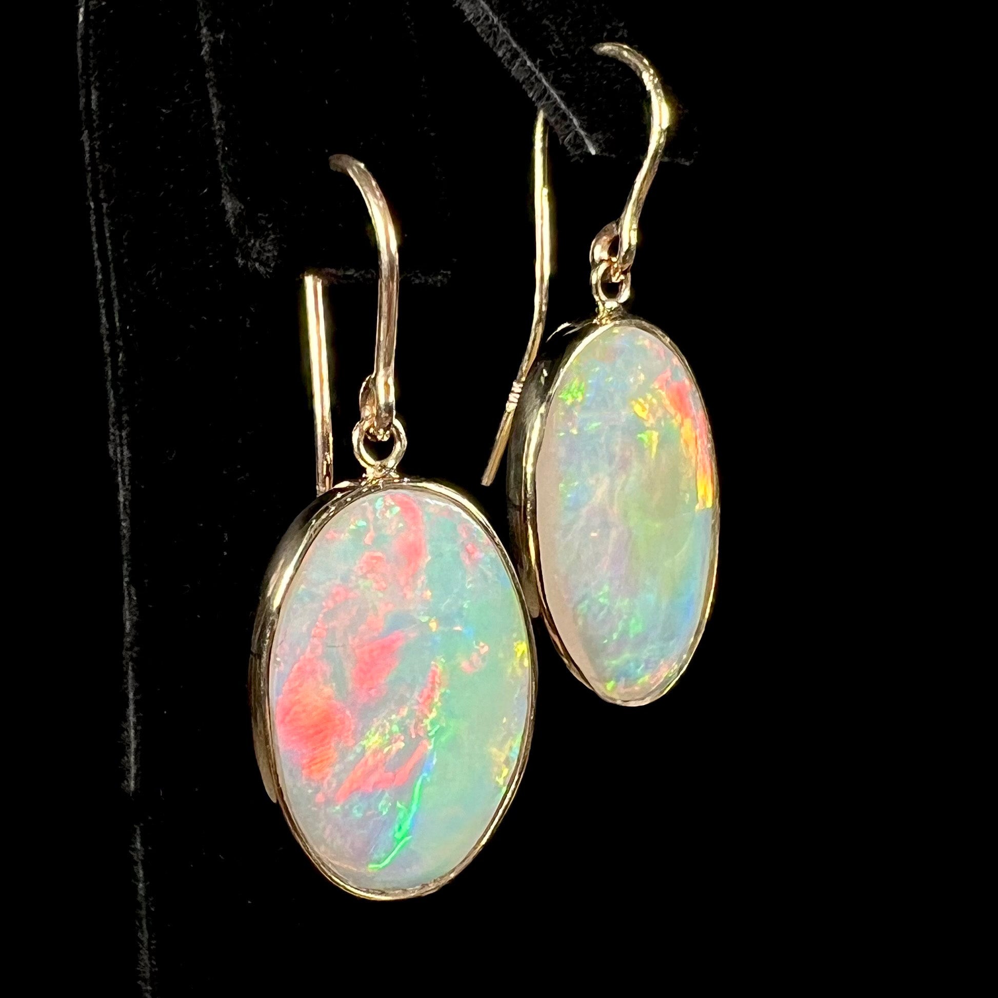 A pair of yellow gold earrings bezel set with oval cabochon cut natural opal stones.