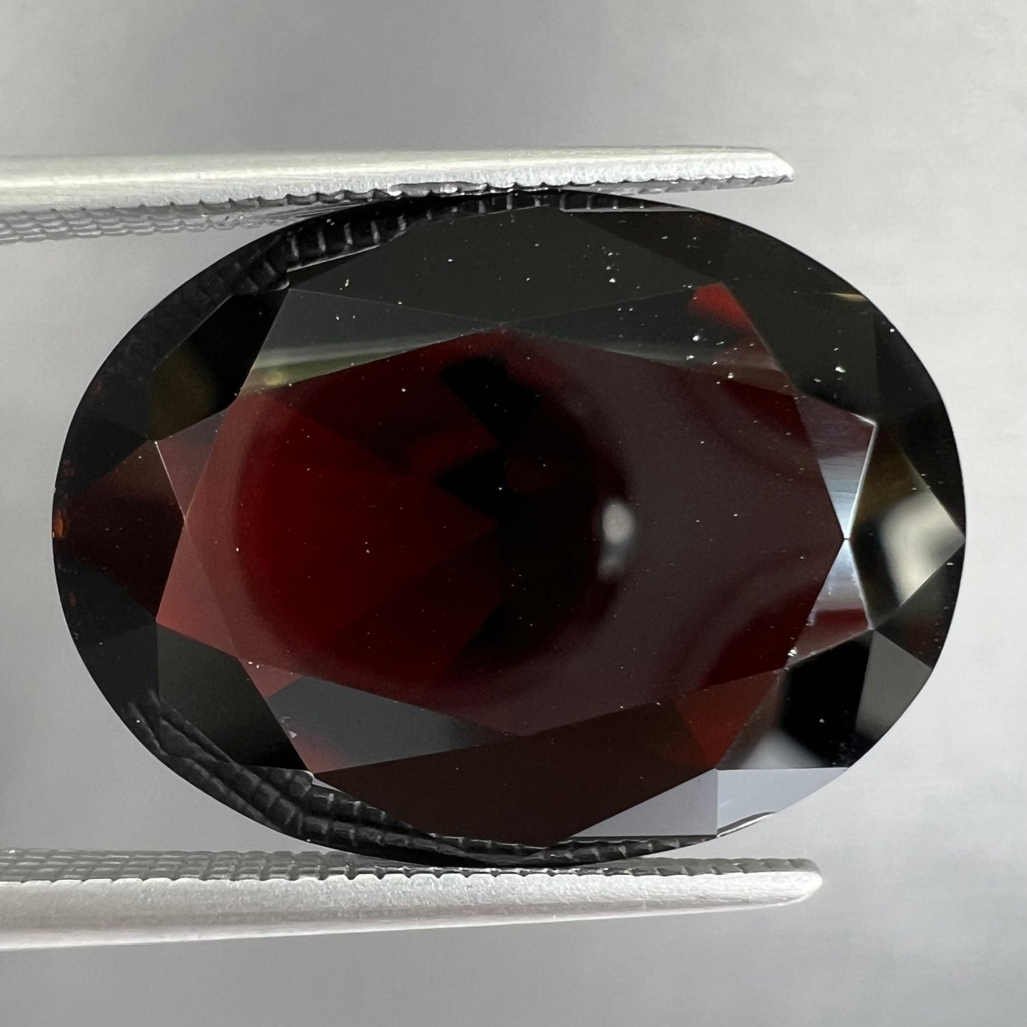 A loose, faceted oval cut pyrope garnet gemstone. The stone is a deep, dark red color.