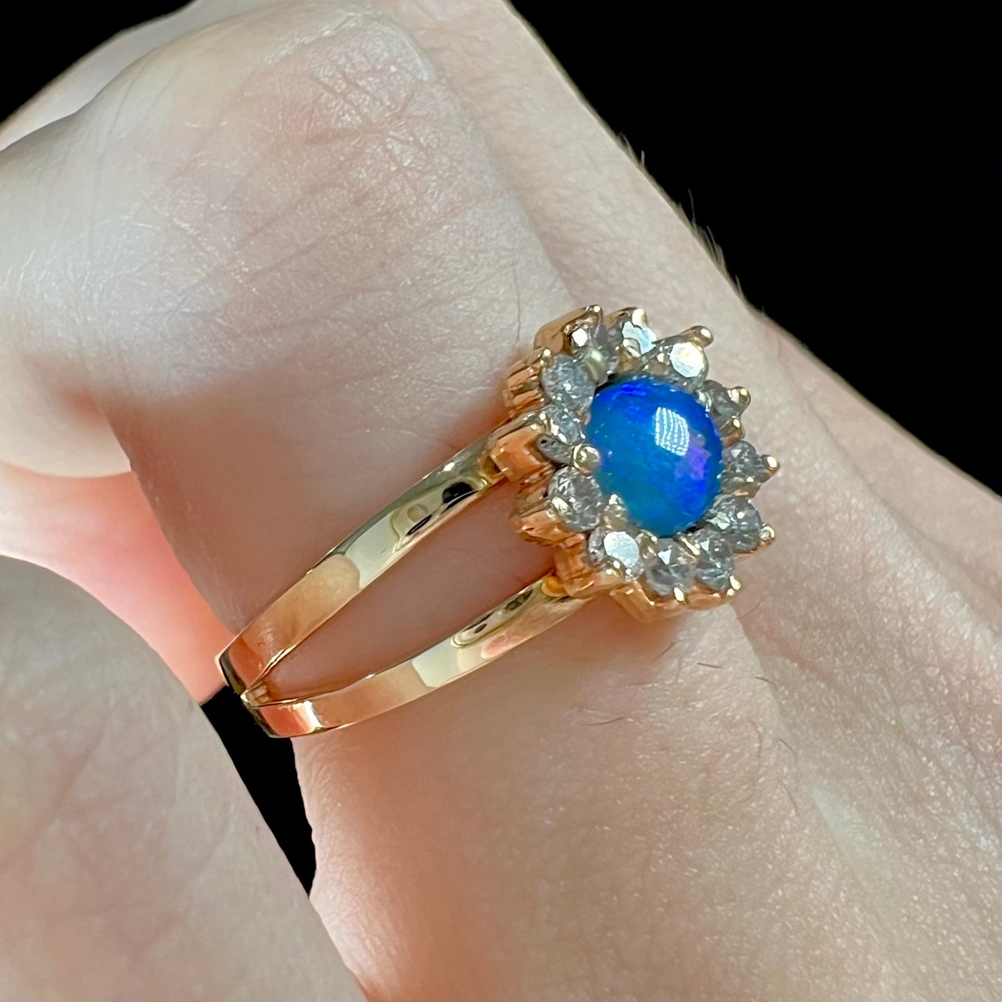 A ladies' round cut black opal and diamond halo ring. The ring is yellow gold and has a split shank.