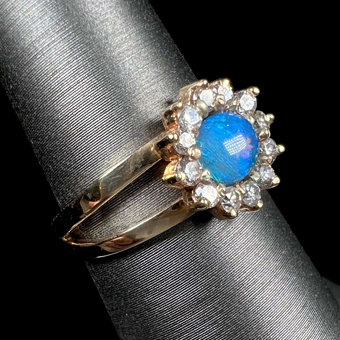A ladies' round cut black opal and diamond halo ring. The ring is yellow gold and has a split shank.