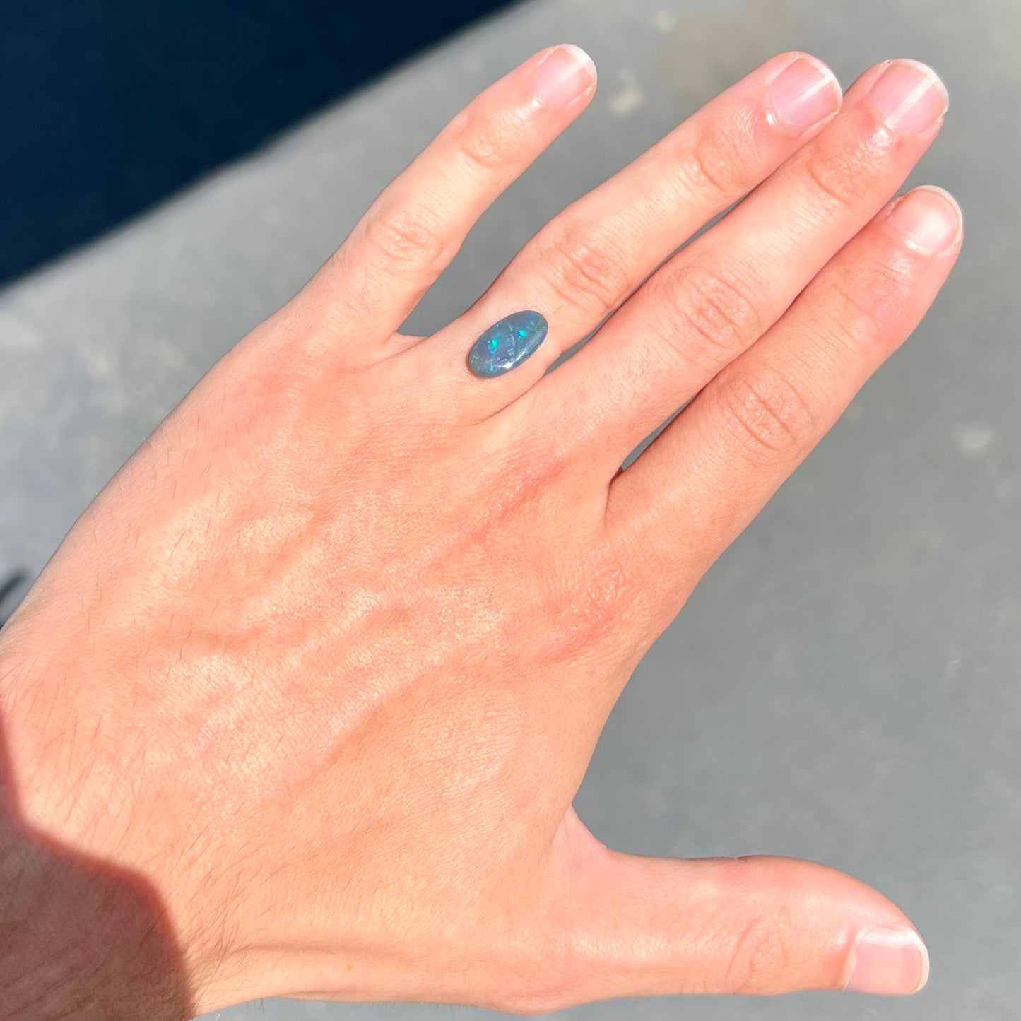 A loose, oval cut black opal stone from Lightning Ridge, Australia. The opal plays with green and blue fire.