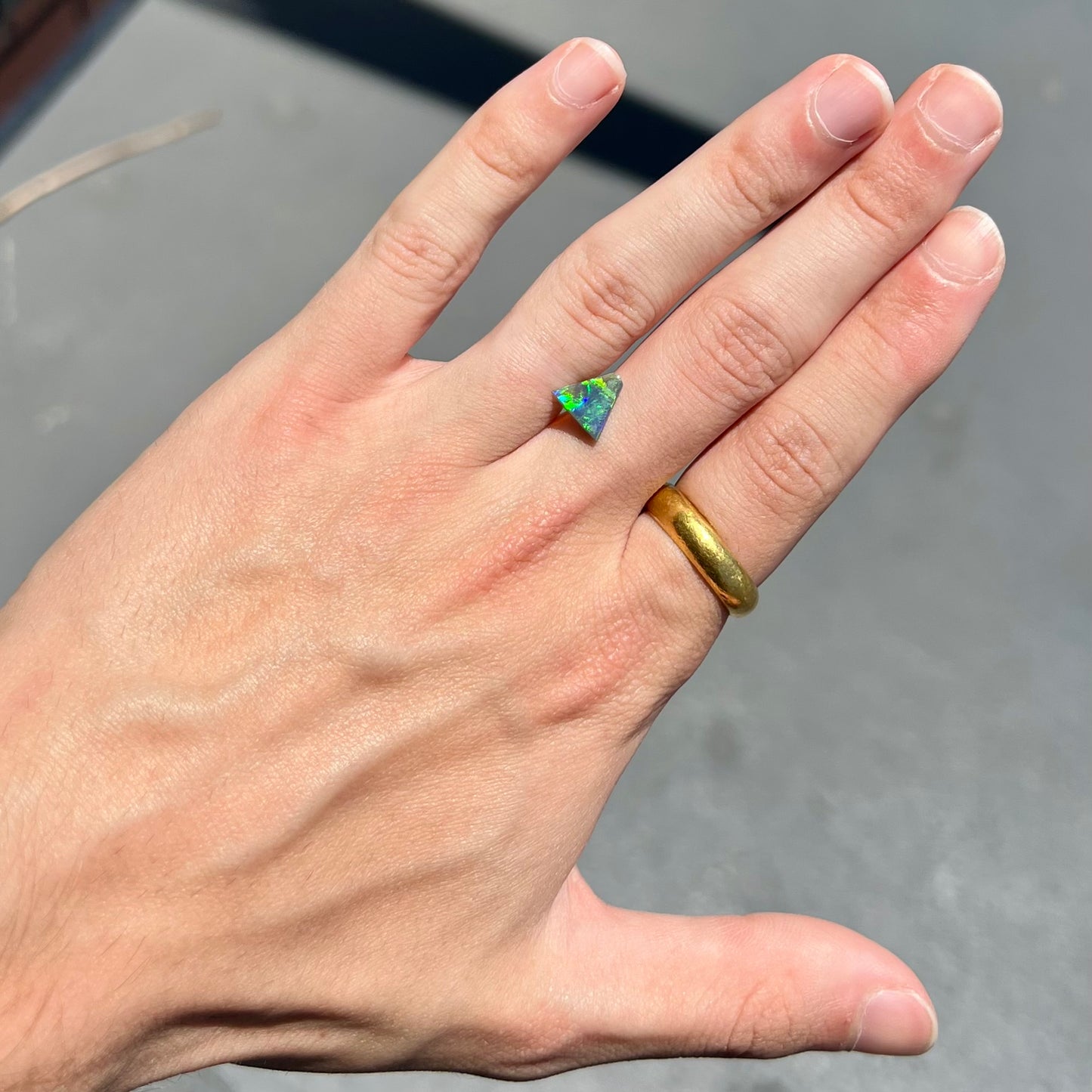 A loose, triangular shaped black opal from Lightning Ride, Australia. The opal is predominantly green.