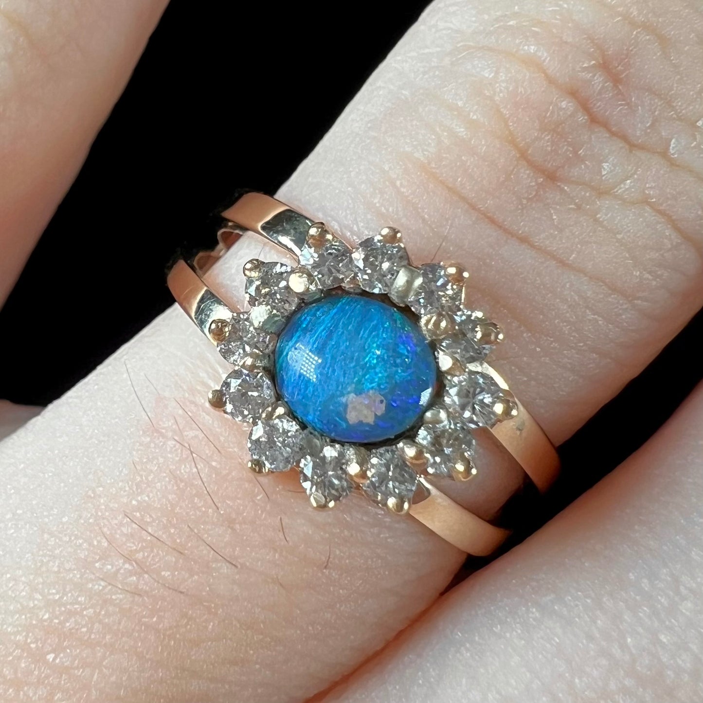 A ladies' round cut black opal and diamond halo ring. The ring is yellow gold and has a split shank.