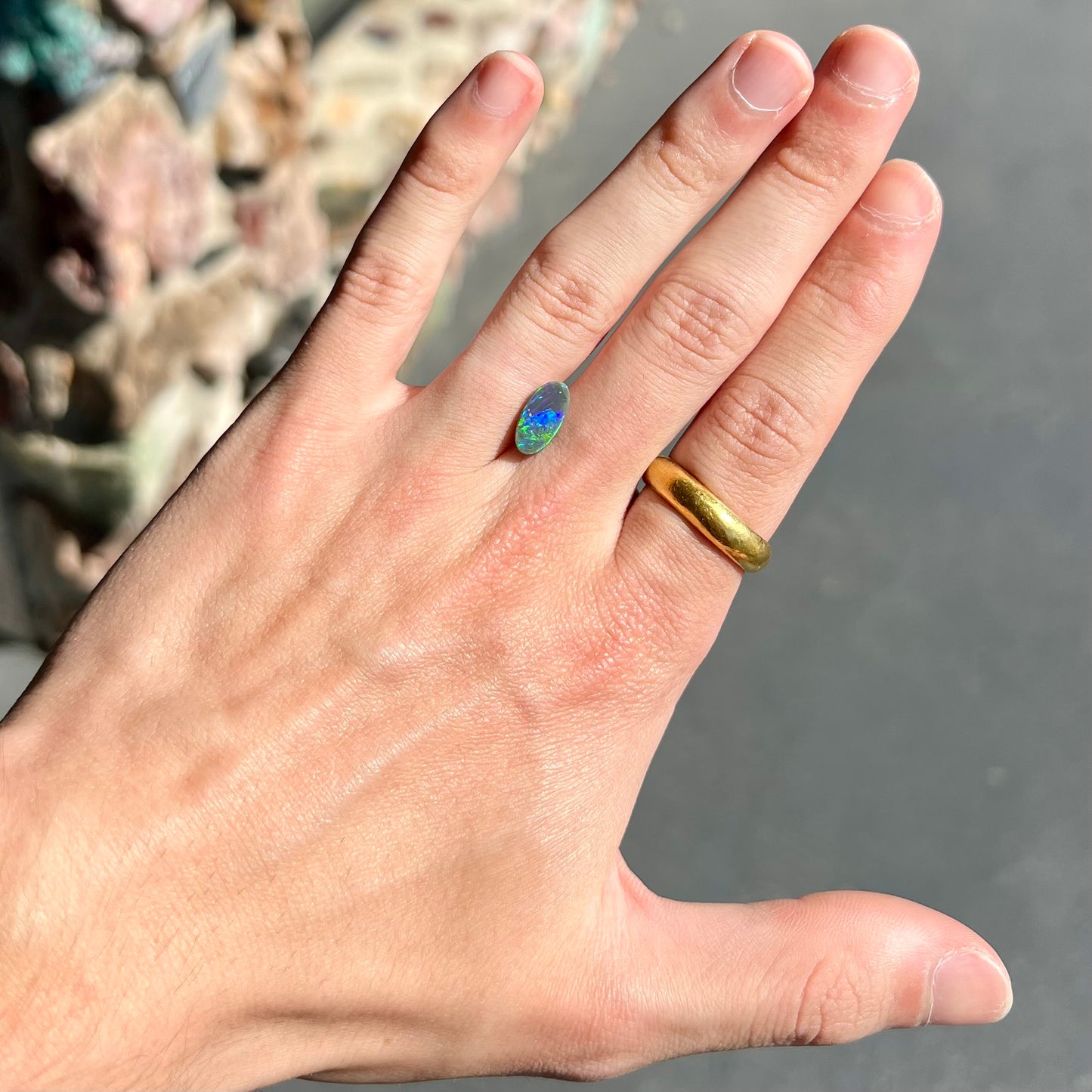 A loose, oval shaped black opal stone from Lightning Ridge, Australia. The opal plays bright green and blue colors.