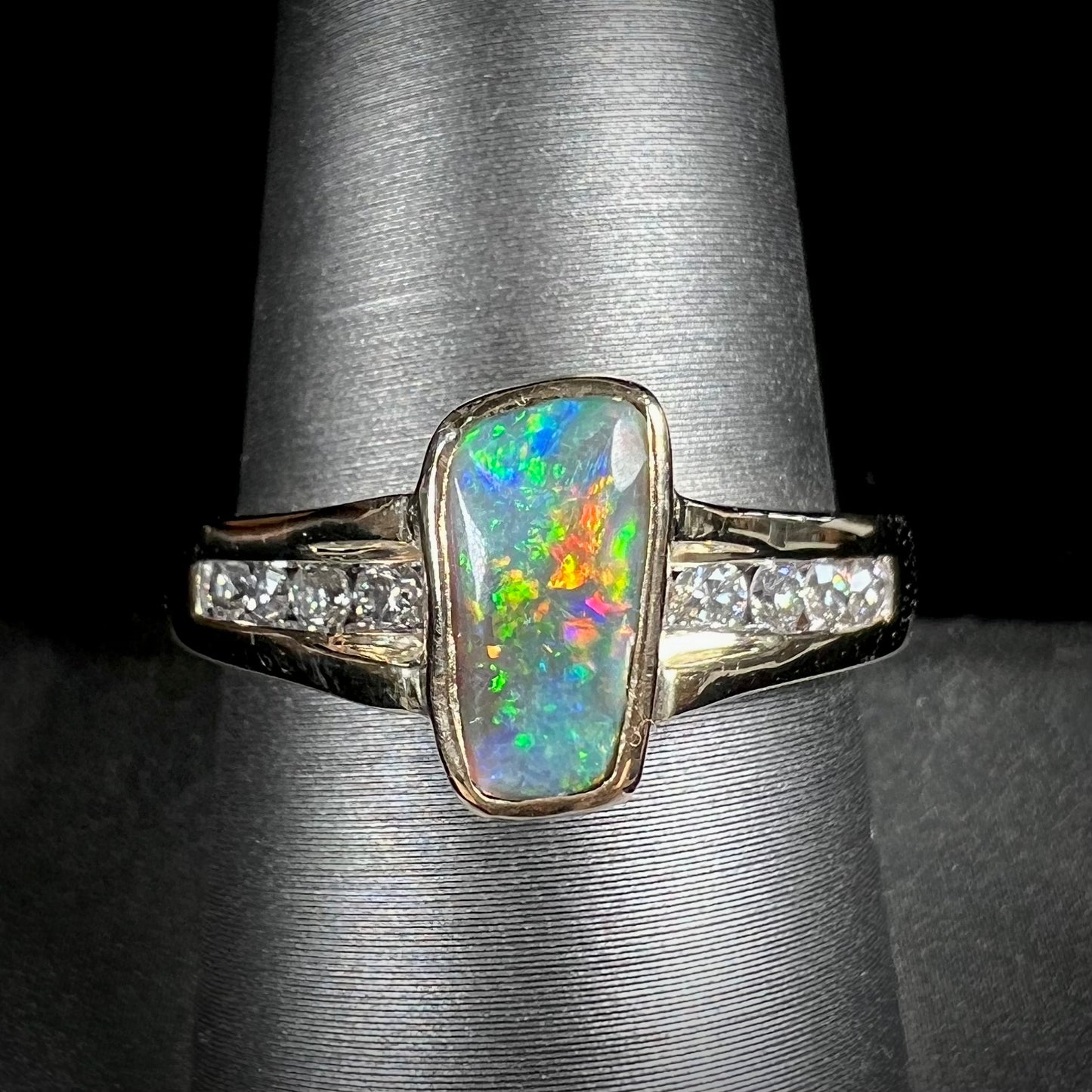 A ladies' yellow gold Australian black crystal opal ring channel set with diamond accent stones.