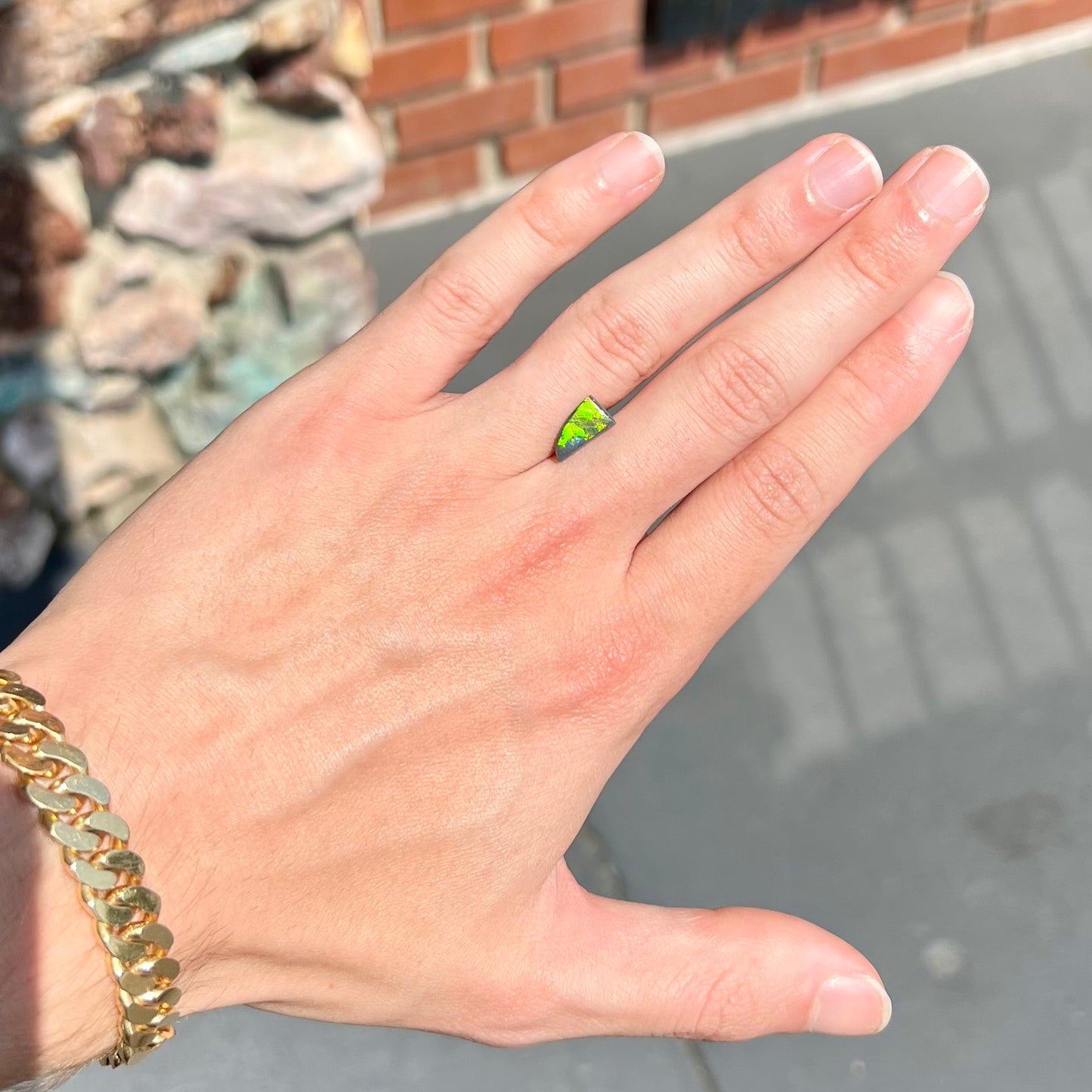 A loose, triangular shaped black opal stone from Lightning Ridge, Australia. The opal has a bright green flash of color.