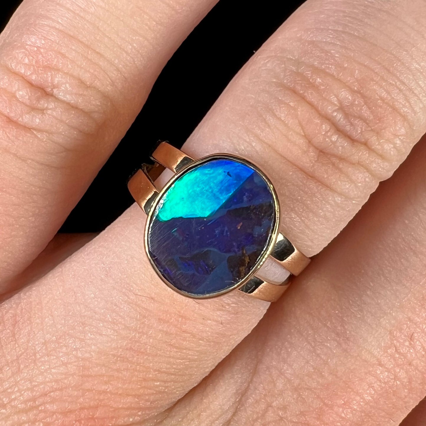 A ladies' split shank natural, Lightning Ridge, Australian black opal solitaire ring in yellow gold.