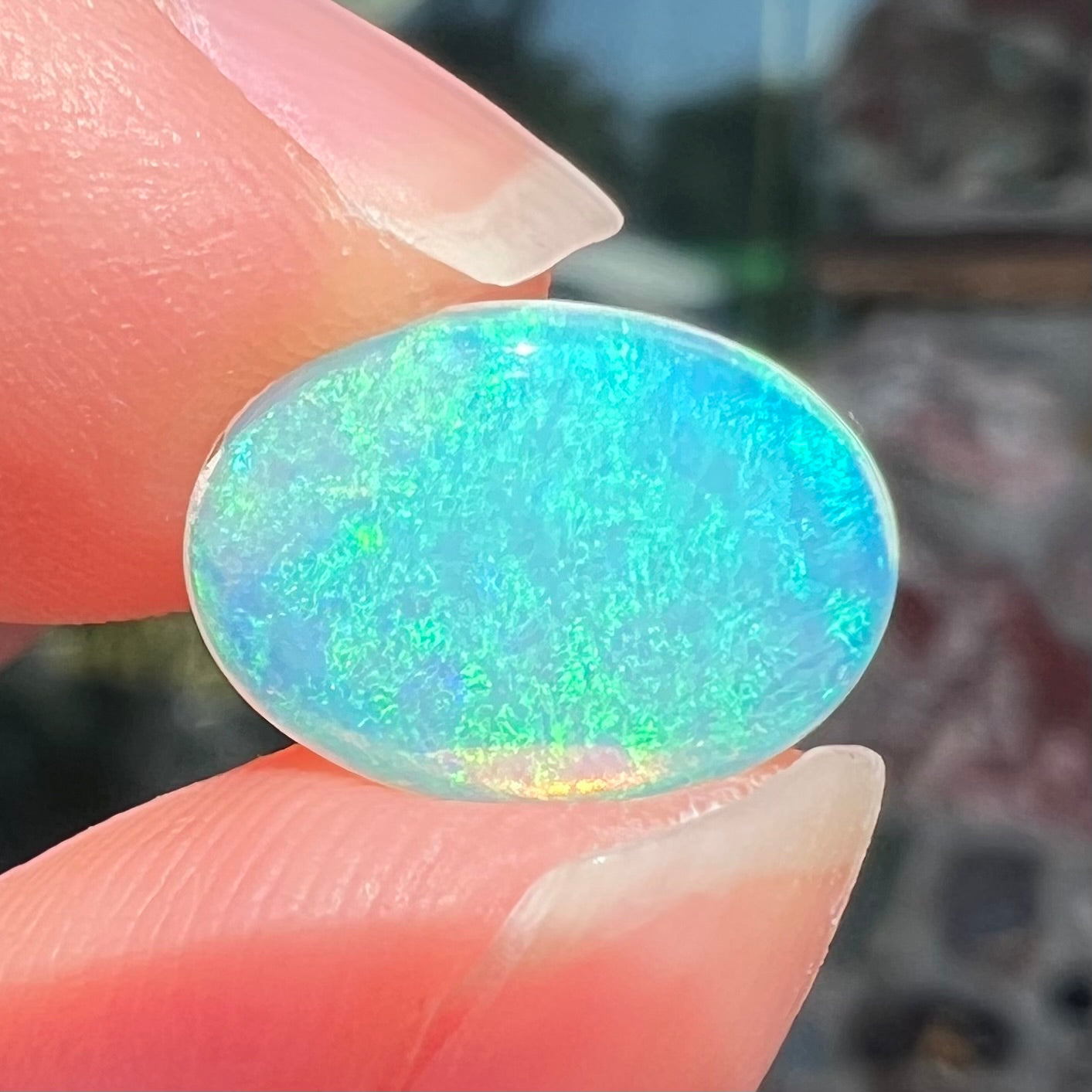 A loose, oval cabochon cut crystal opal from Coober Pedy, Australia. The opal has green and blue colors.